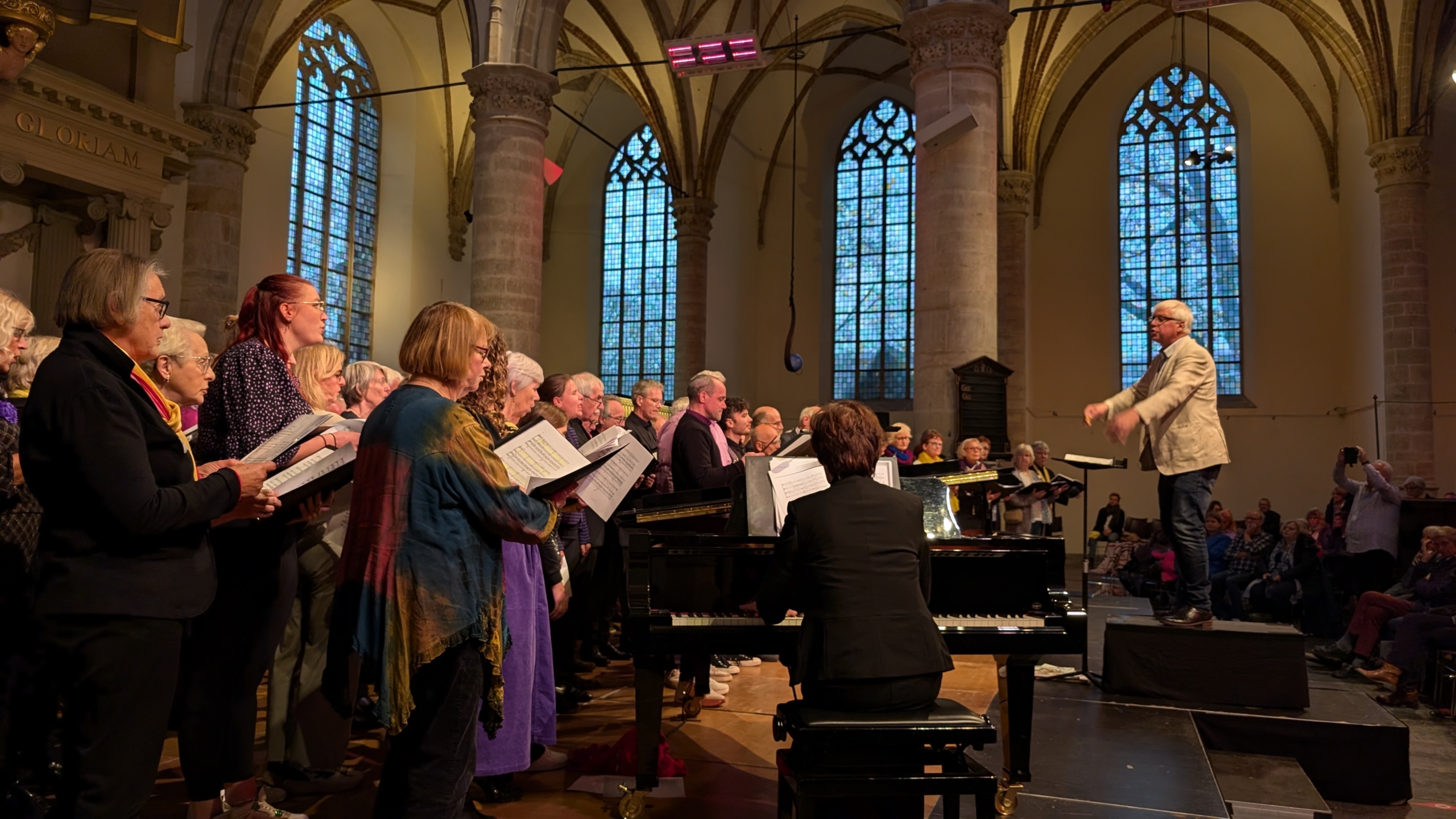 Kooroptreden in een kerk met een dirigent en een pianist.