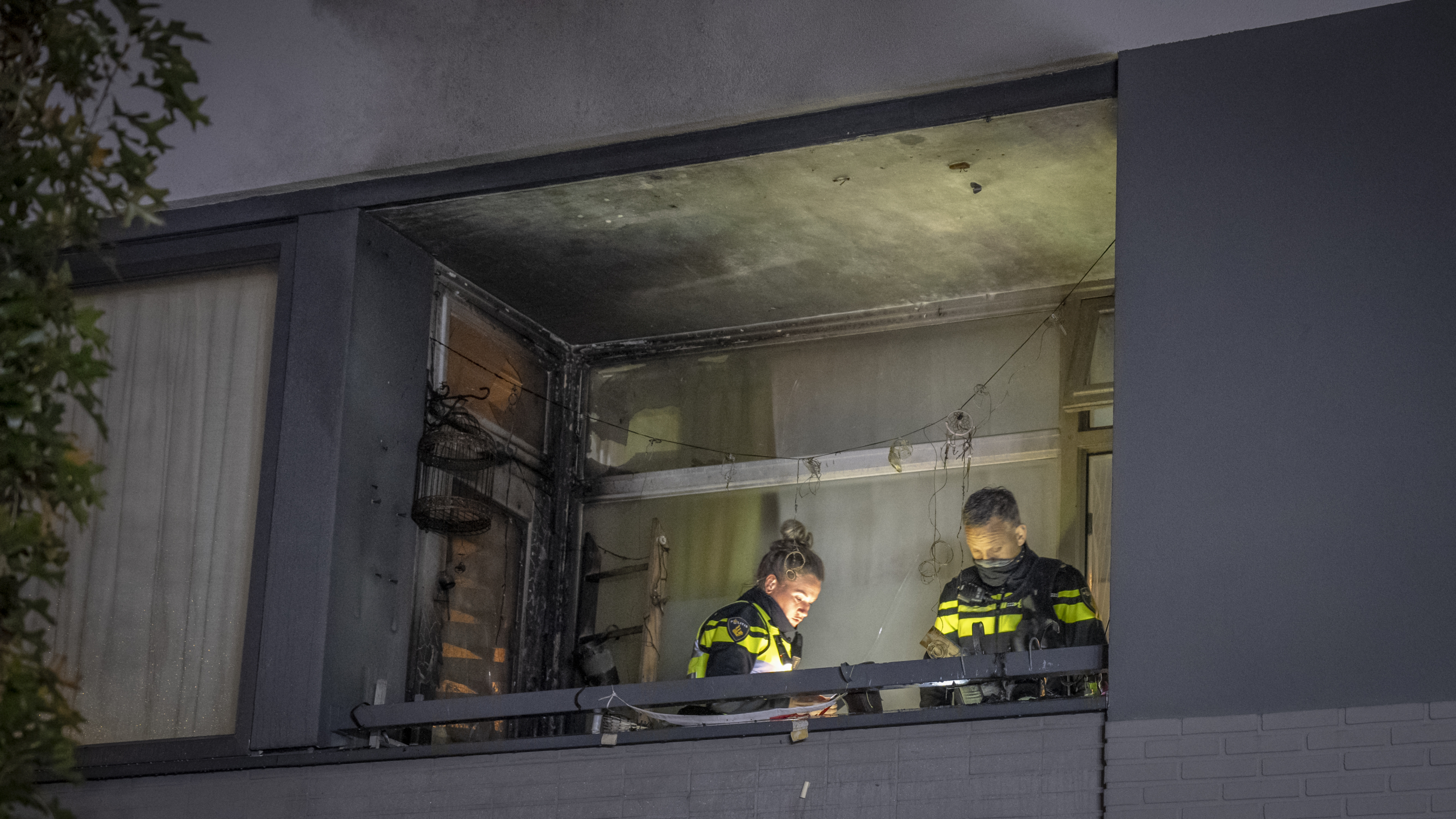 Twee politieagenten onderzoeken een door brand beschadigd balkon.