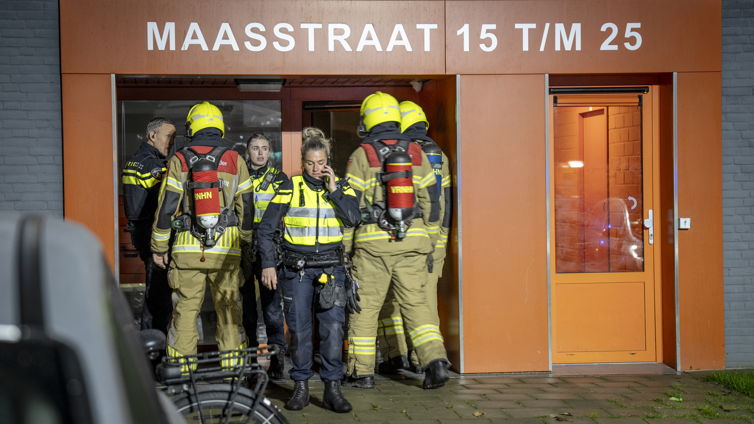 Brandweerlieden en politieagenten bij ingang van een gebouw op de Maasstraat 15 t/m 25.