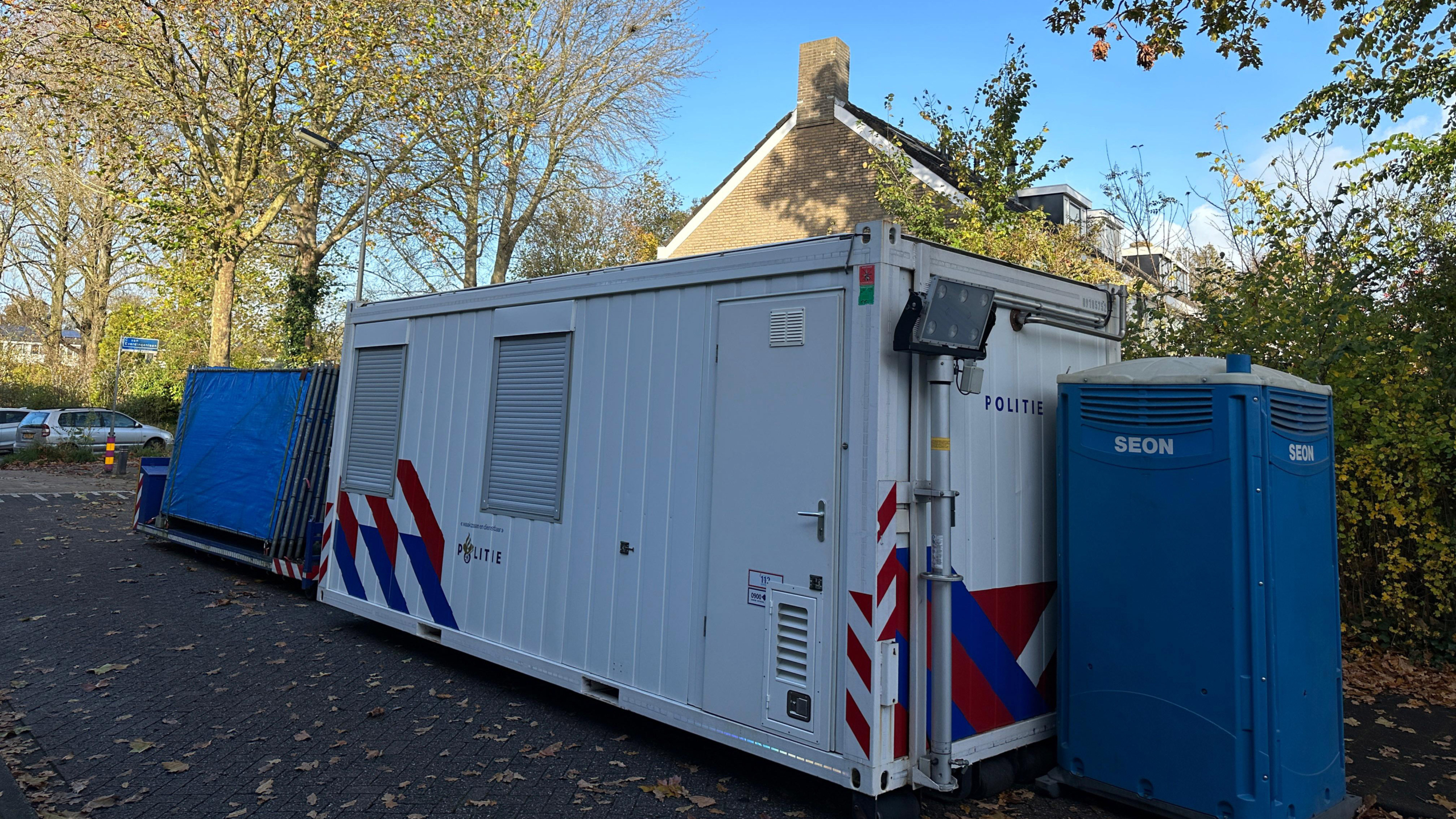 Mobiele politie-eenheid met container en bouwtoilet op straat.