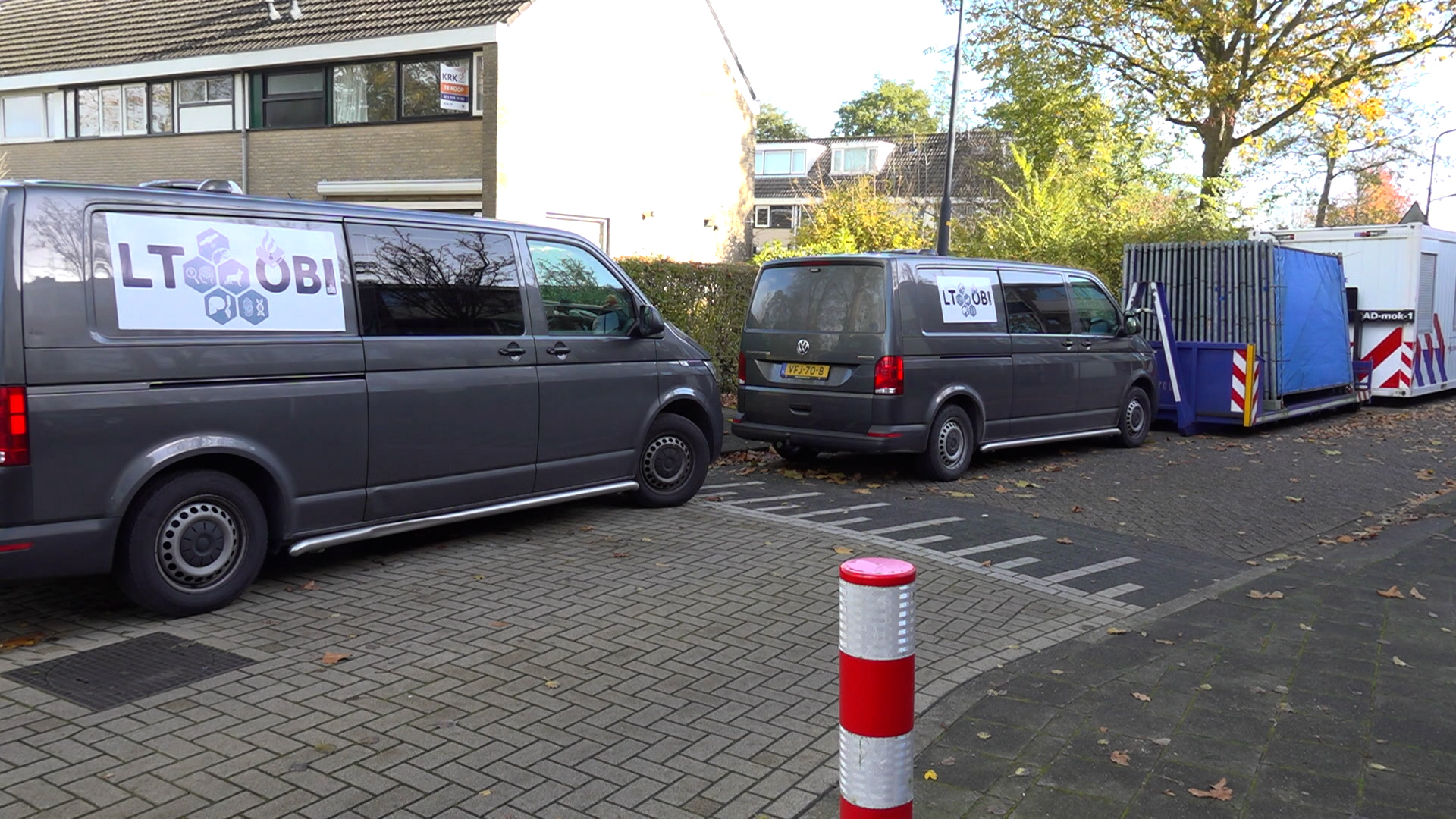 Grijze bestelwagens met daarop het logo van LT OBI staan geparkeerd op een straat naast een groot blauw afgedekt object.