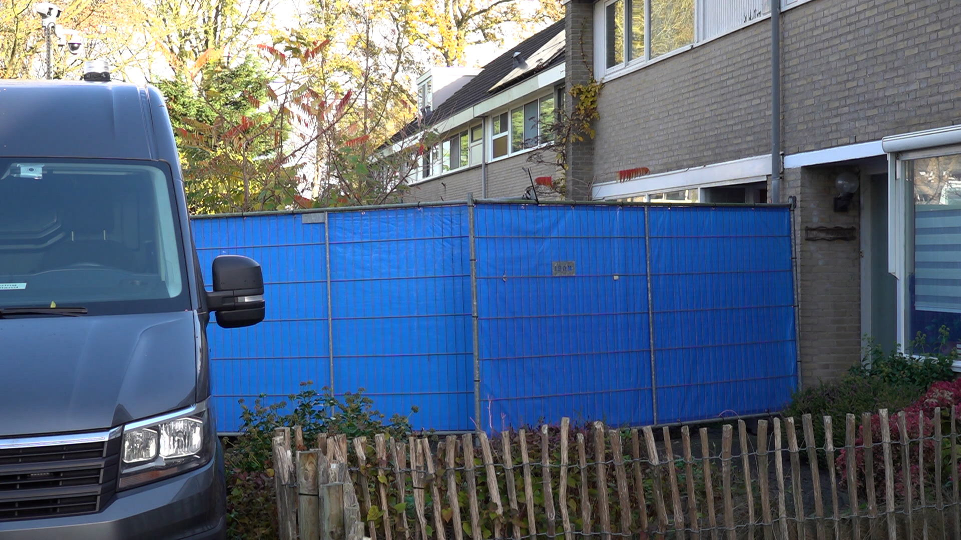 Blauwe bouwhekpanelen rond een huis met een grijze bestelwagen op de voorgrond.