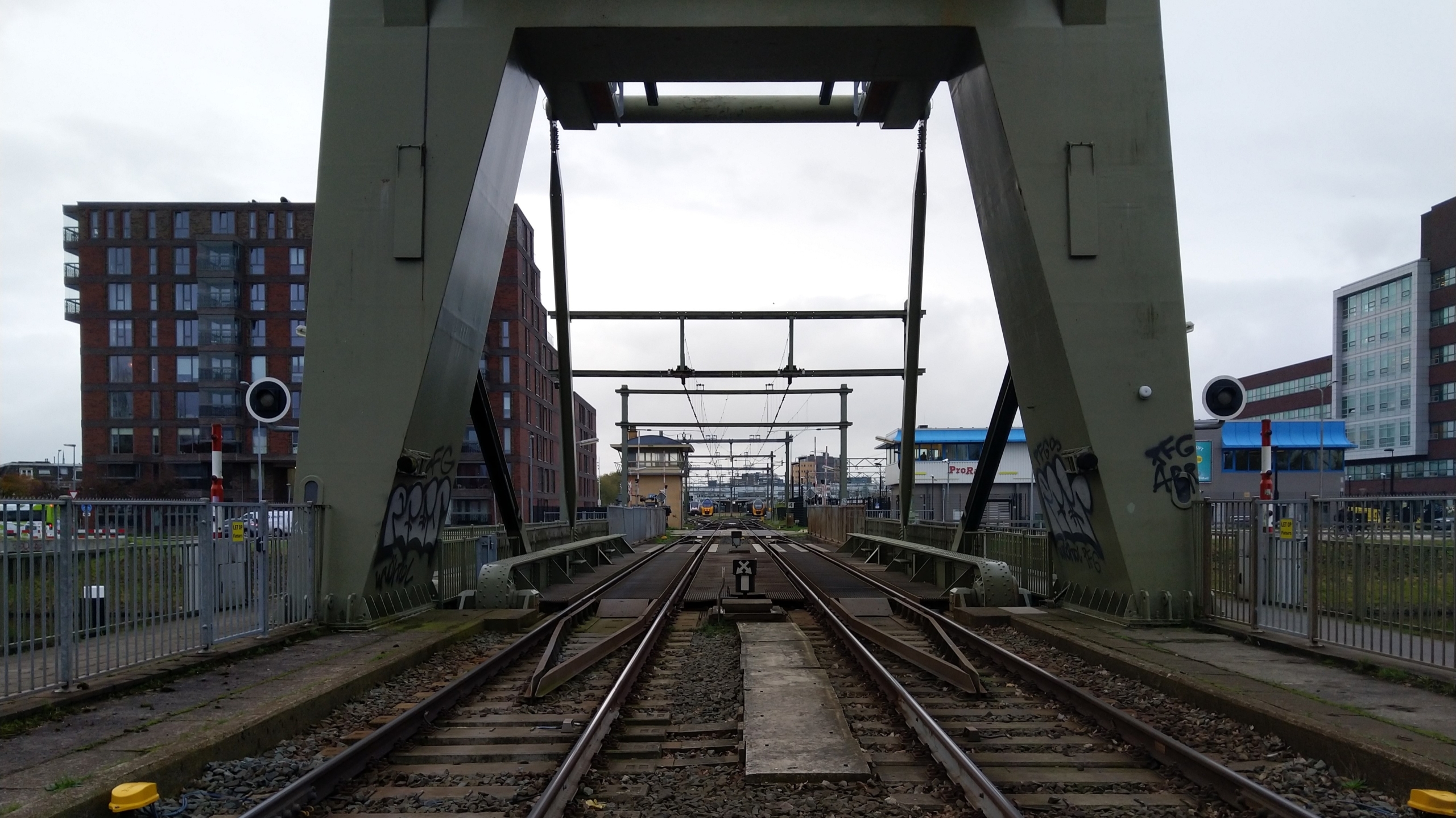 Spoorbrug met rails, omgeven door gebouwen en elektriciteitsmasten.