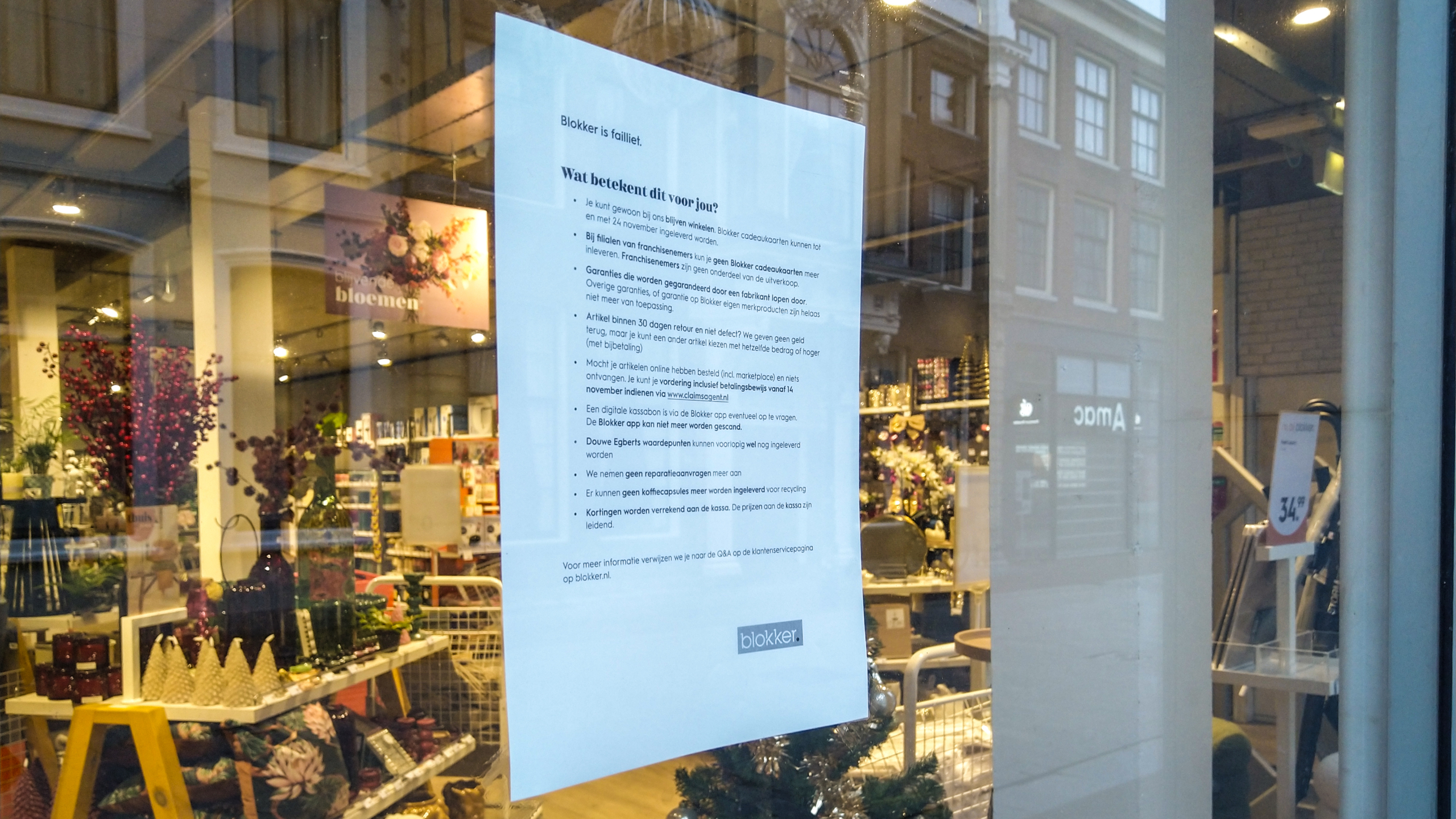 Een poster op een etalageraam met informatie over een faillissement, met op de achtergrond een winkel met huishoudelijke artikelen en decoraties.