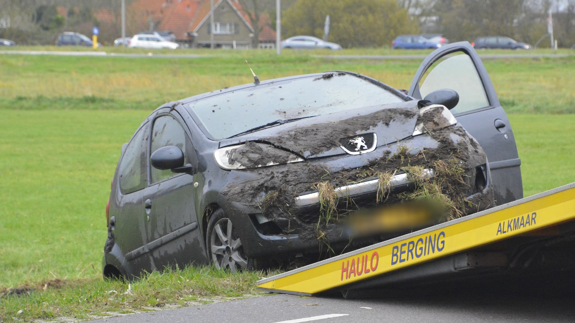 Zwarte auto met modder schade aan de voorkant op een bergingswagen in een grasveld.