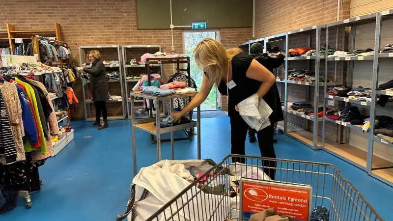 Een kledingbank met twee vrouwen die kleding sorteren en op de planken leggen.