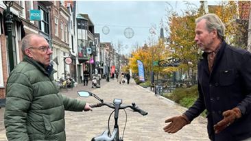 Twee mannen hebben een gesprek op een straat met bakstenen en herfstbomen.