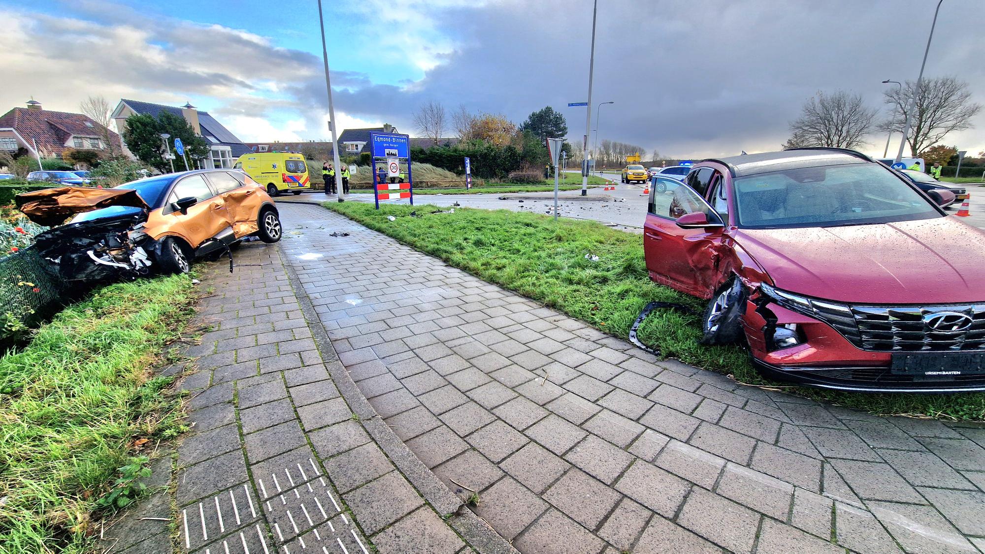 Twee auto's met ernstige schade na botsing, omringd door politie en ambulancemedewerkers op een rotonde.