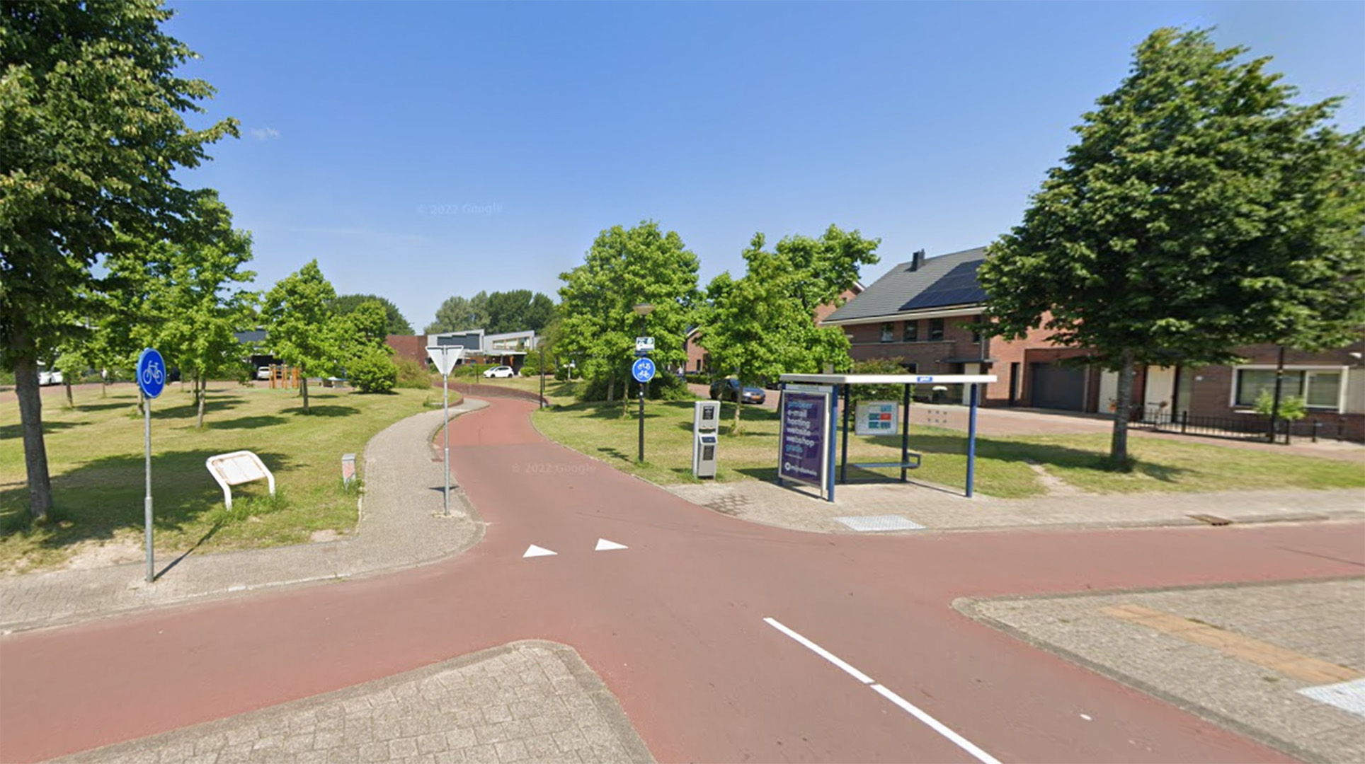 Een rustige straat met rood fietspad, omringd door groene bomen en een bushalte aan de rechterkant.