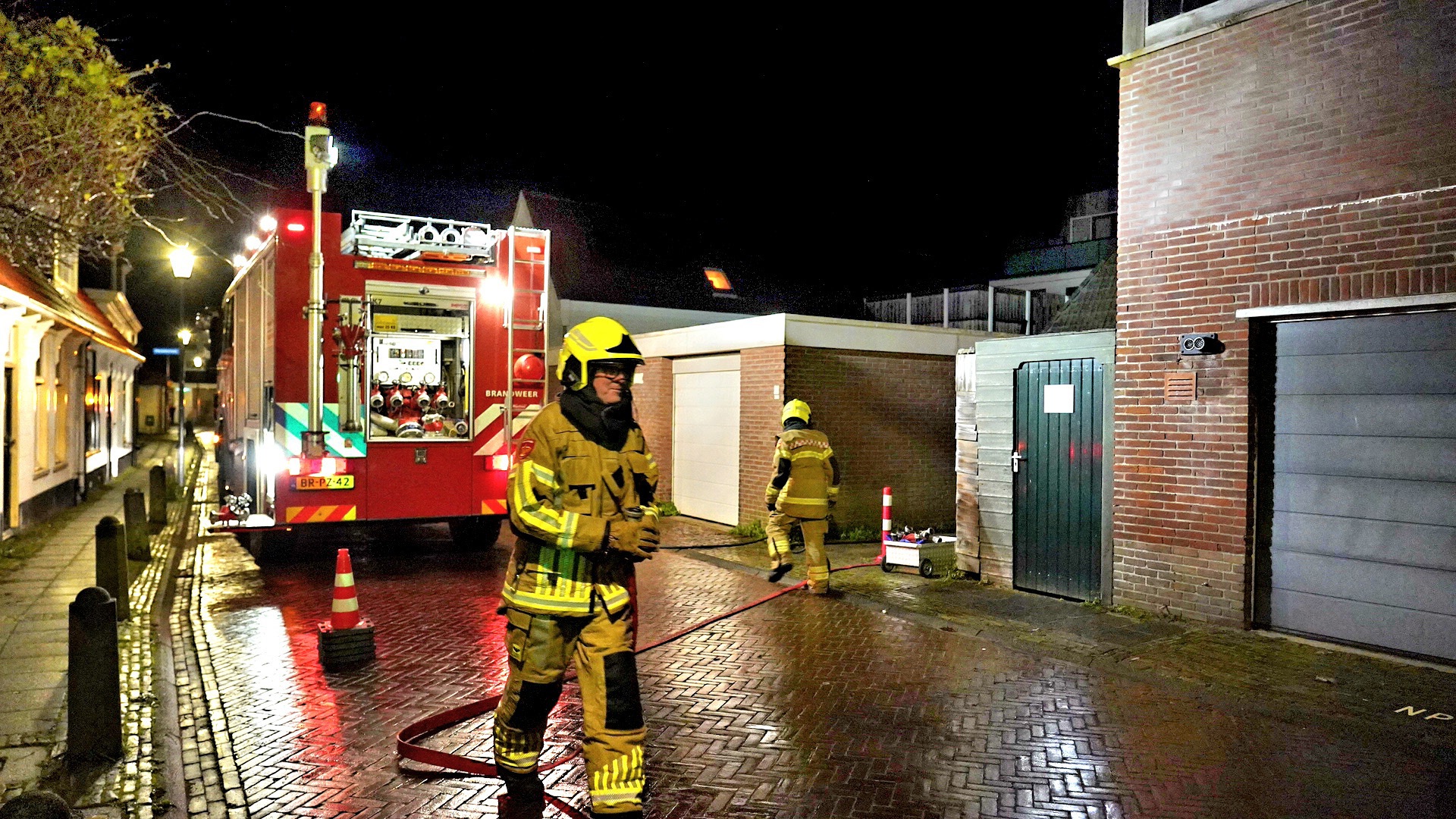 Brandweerlieden bij een brandweerwagen in een straat tijdens de nacht.