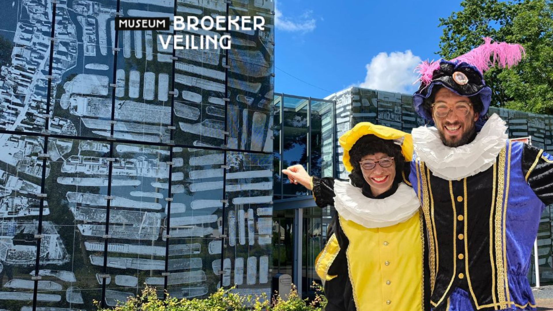 Twee mensen in traditionele kleding poseren lachend voor het Museum BroekerVeiling.