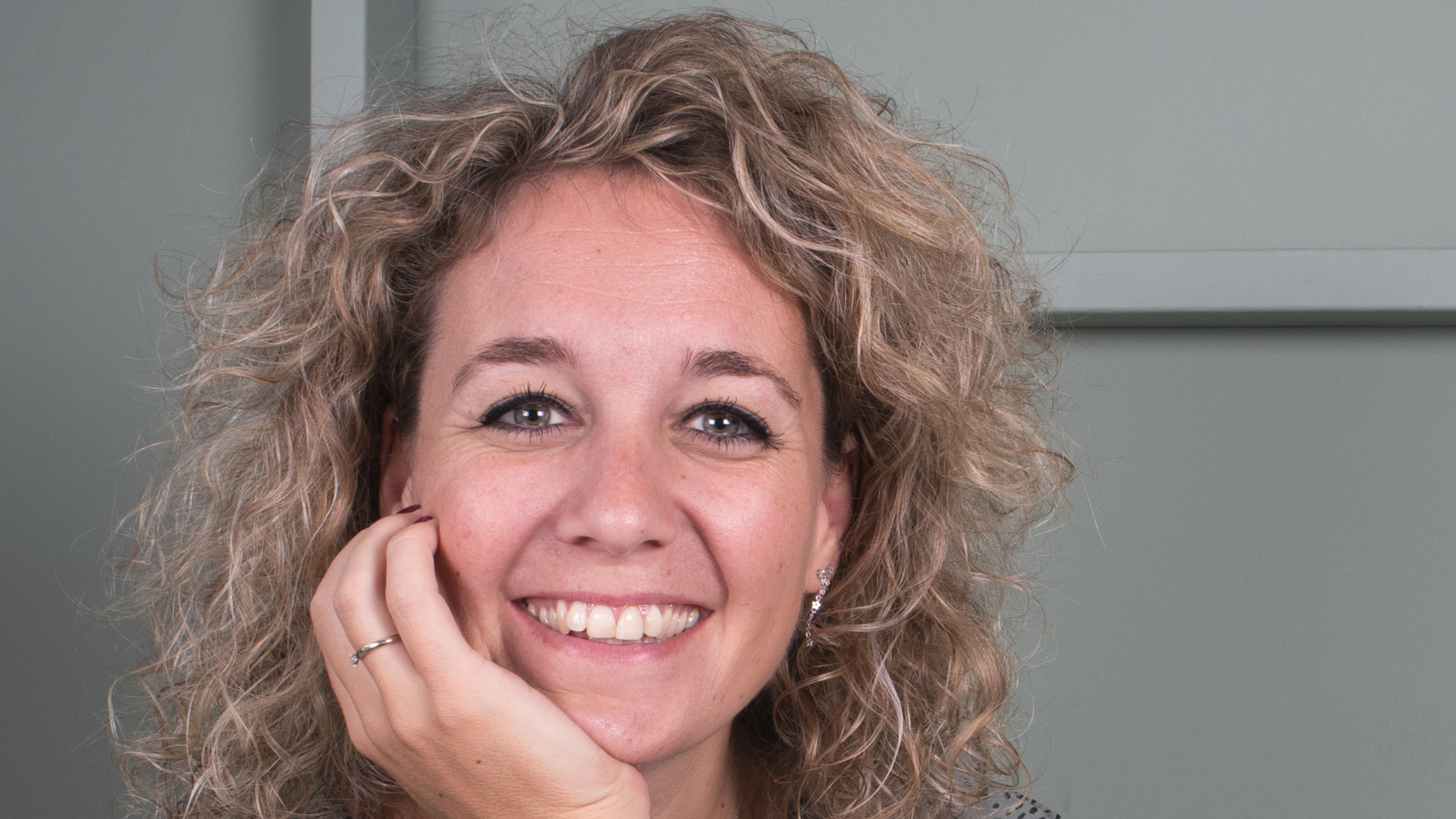 Vrouw met krullend blond haar en polkadot blouse glimlacht naar de camera.