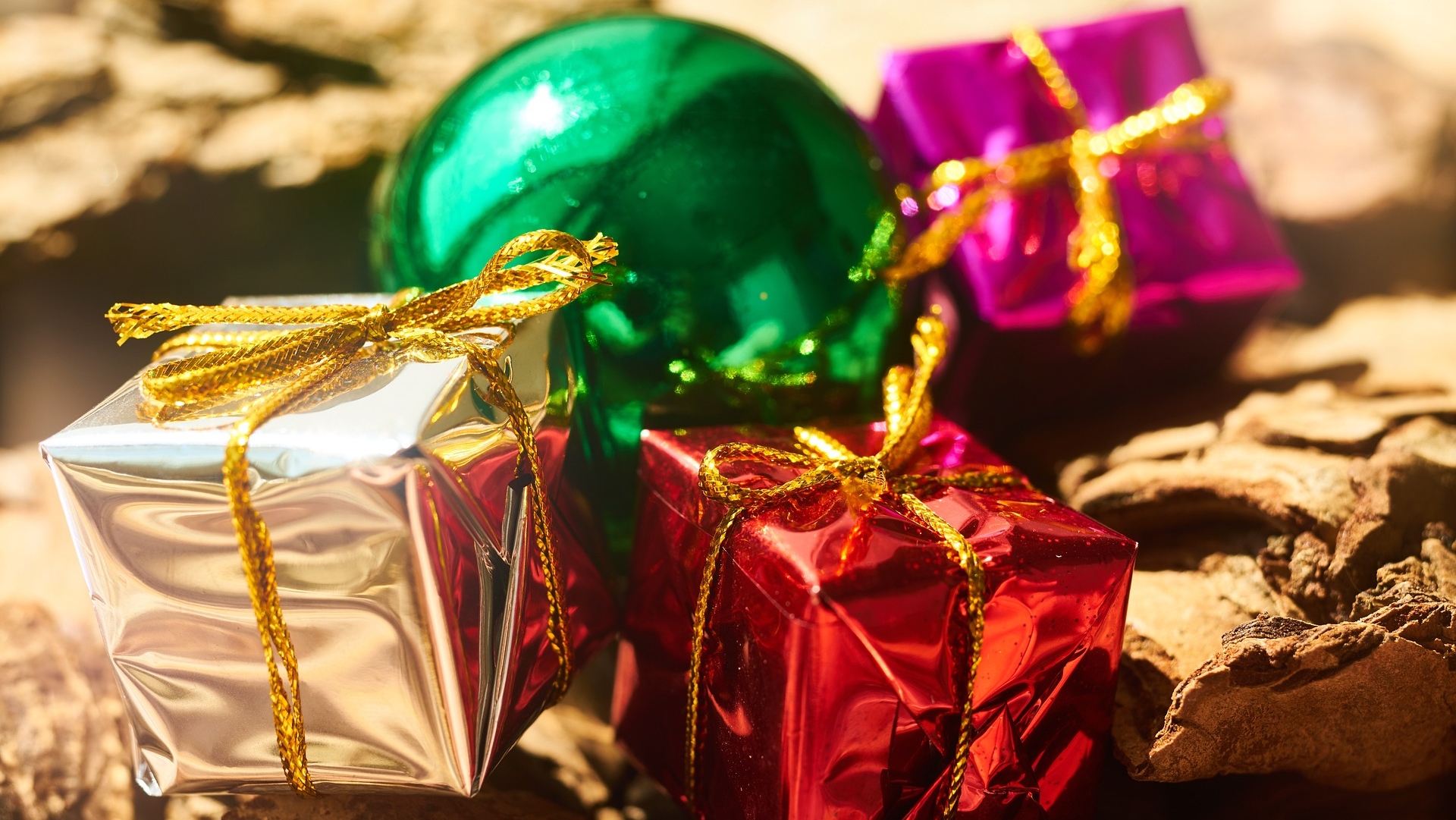 Gekleurde cadeauverpakkingen met gouden linten en een groene kerstbal op een achtergrond van schors.