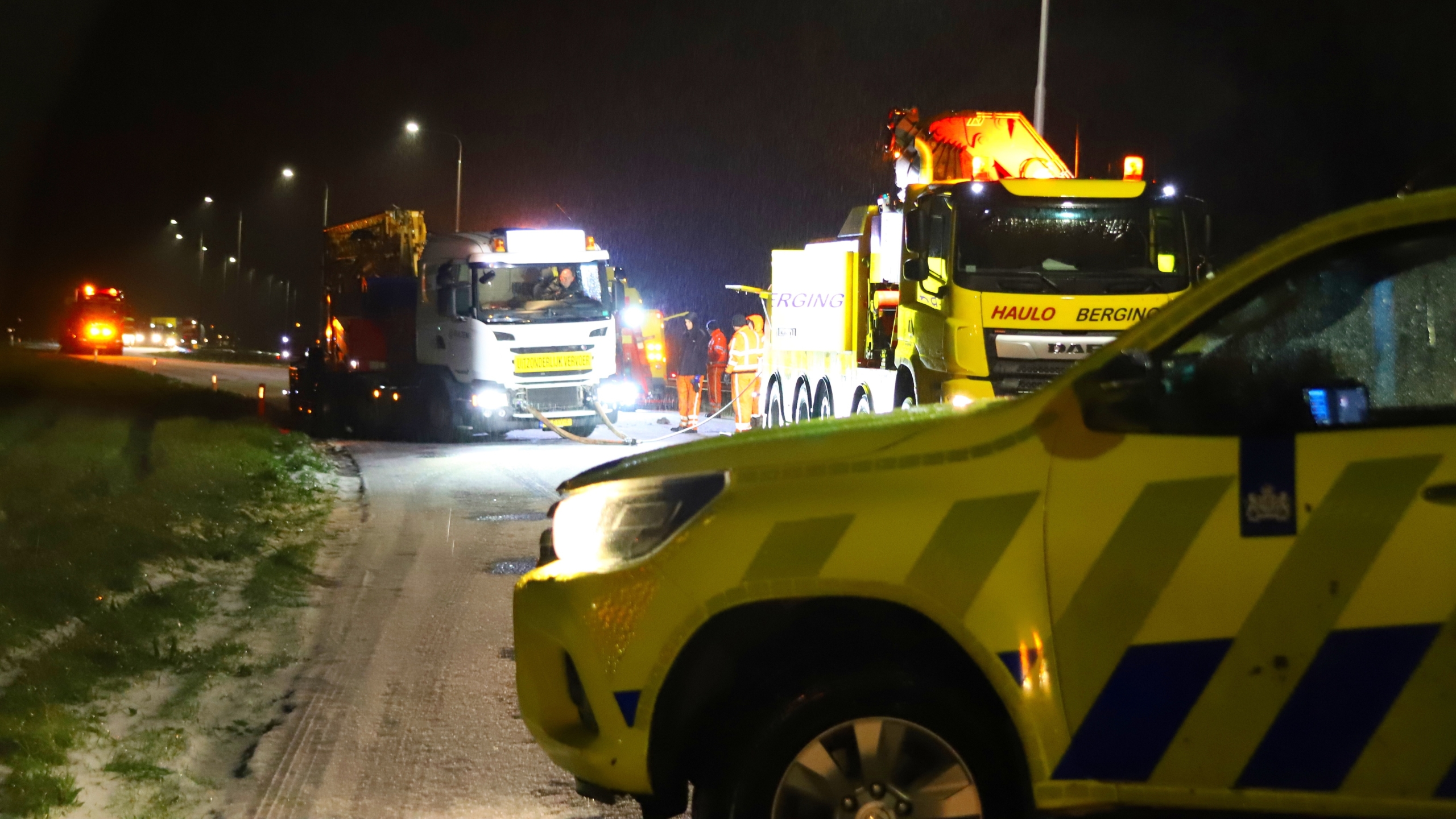 Vrachtwagens en voertuigen werken 's nachts op een verlichte weg.