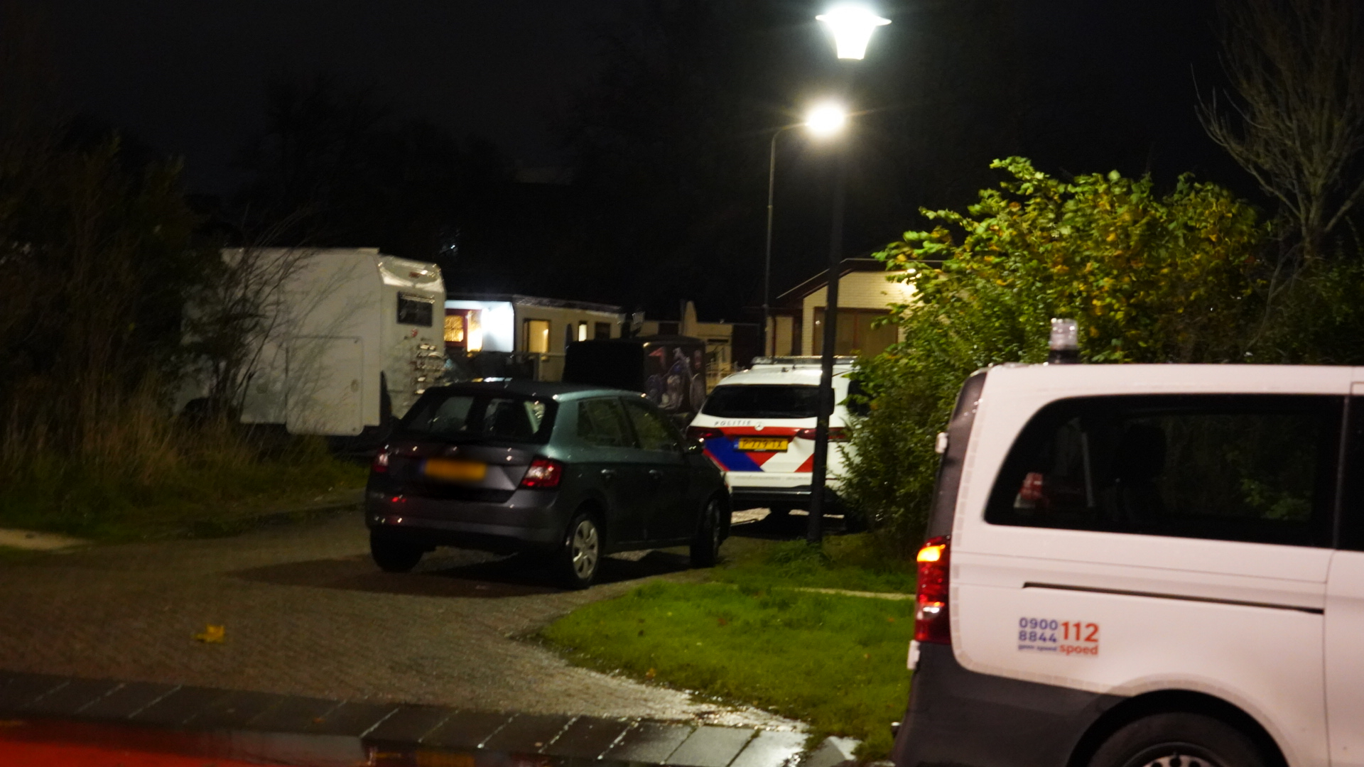 Politievoertuigen en geparkeerde auto's op een donkere weg bij avond.