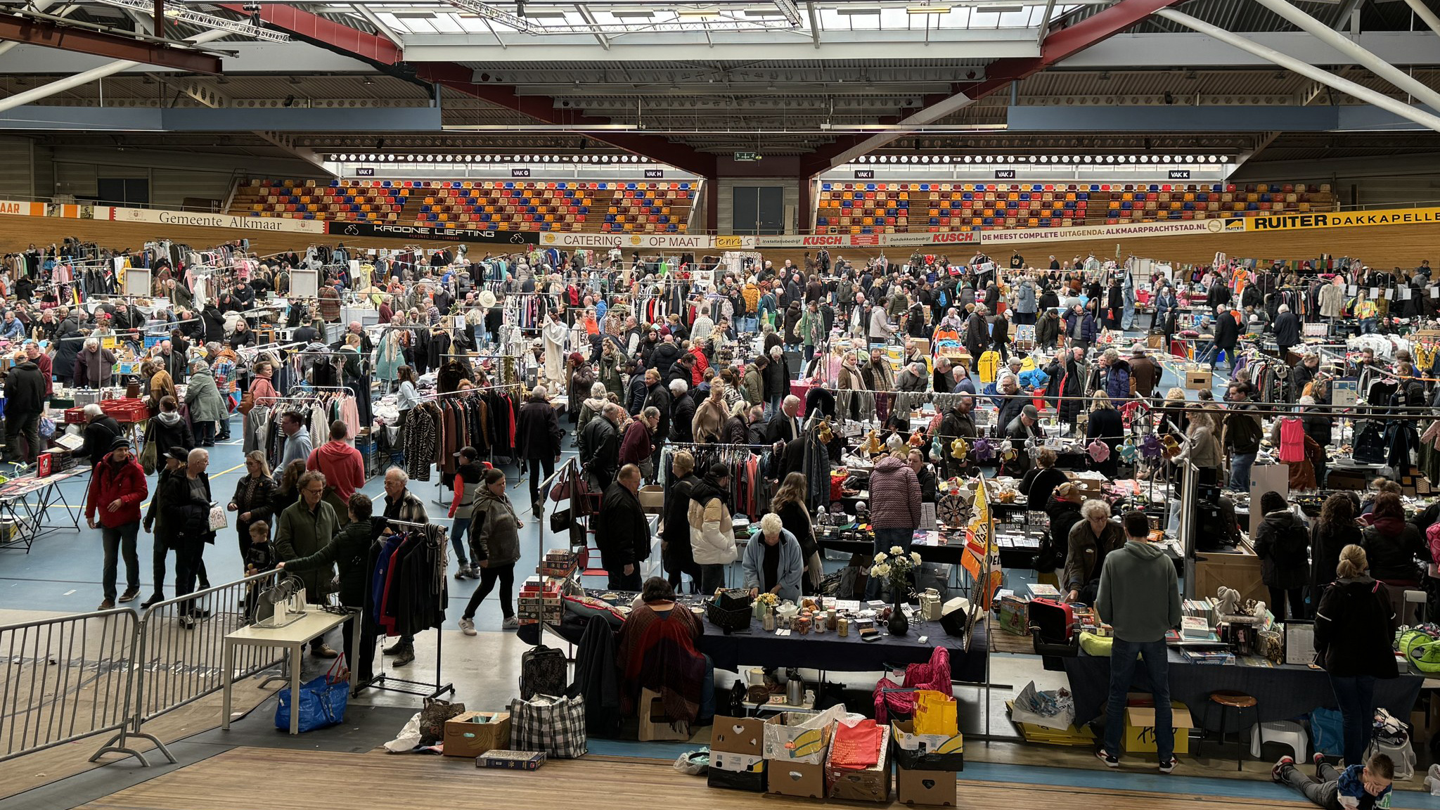 Drukke vlooienmarkt in een grote sporthal met veel mensen en kraampjes.