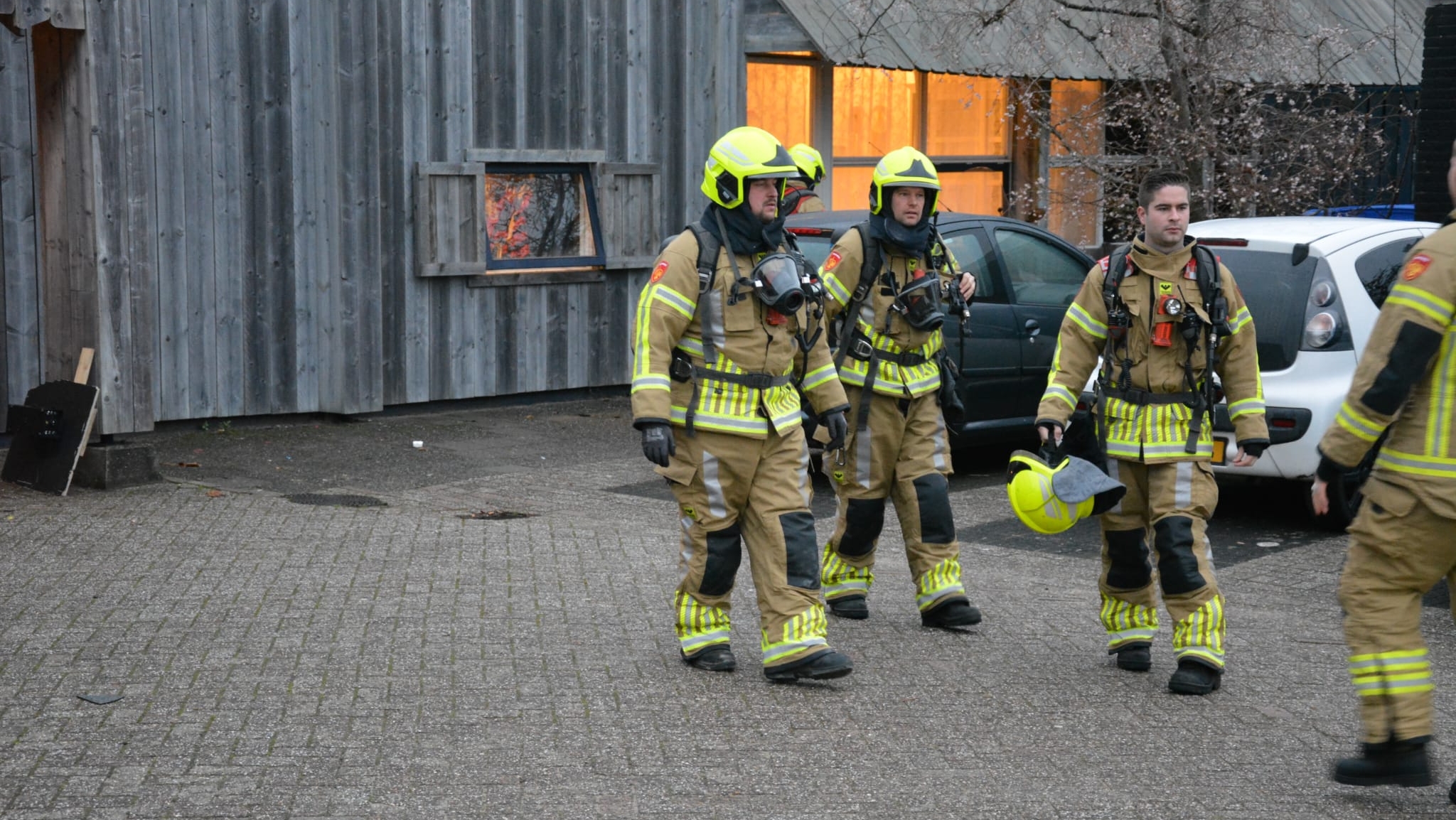 Brandweerlieden in beschermende kleding lopen buiten bij een gebouw.