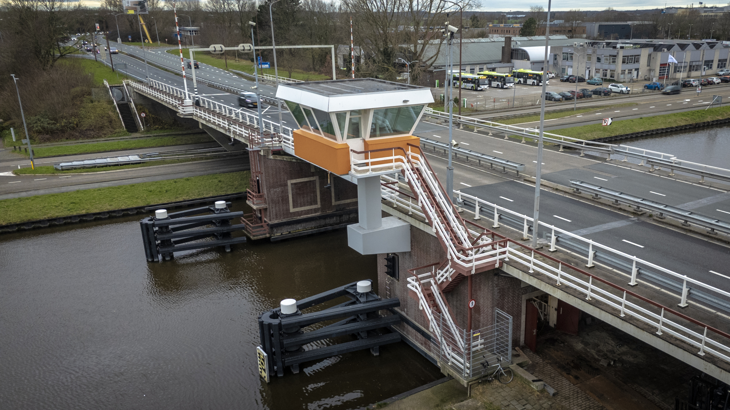 Een draaibrug over een kanaal met een bedieningshuisje erboven, omringd door wegen en gebouwen.