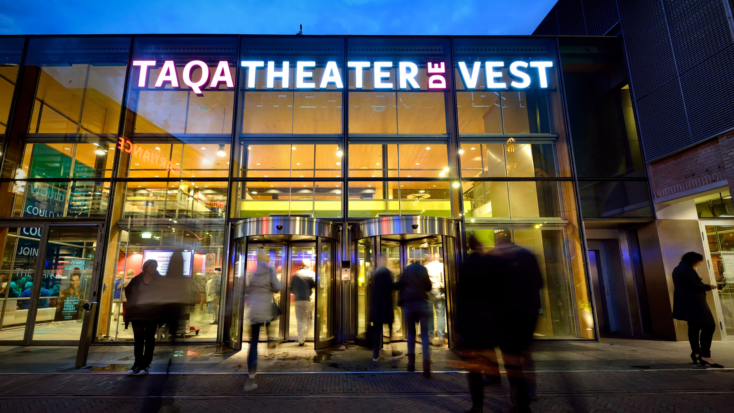 Ingang van het TAQA Theater De Vest met mensen die naar binnen gaan.