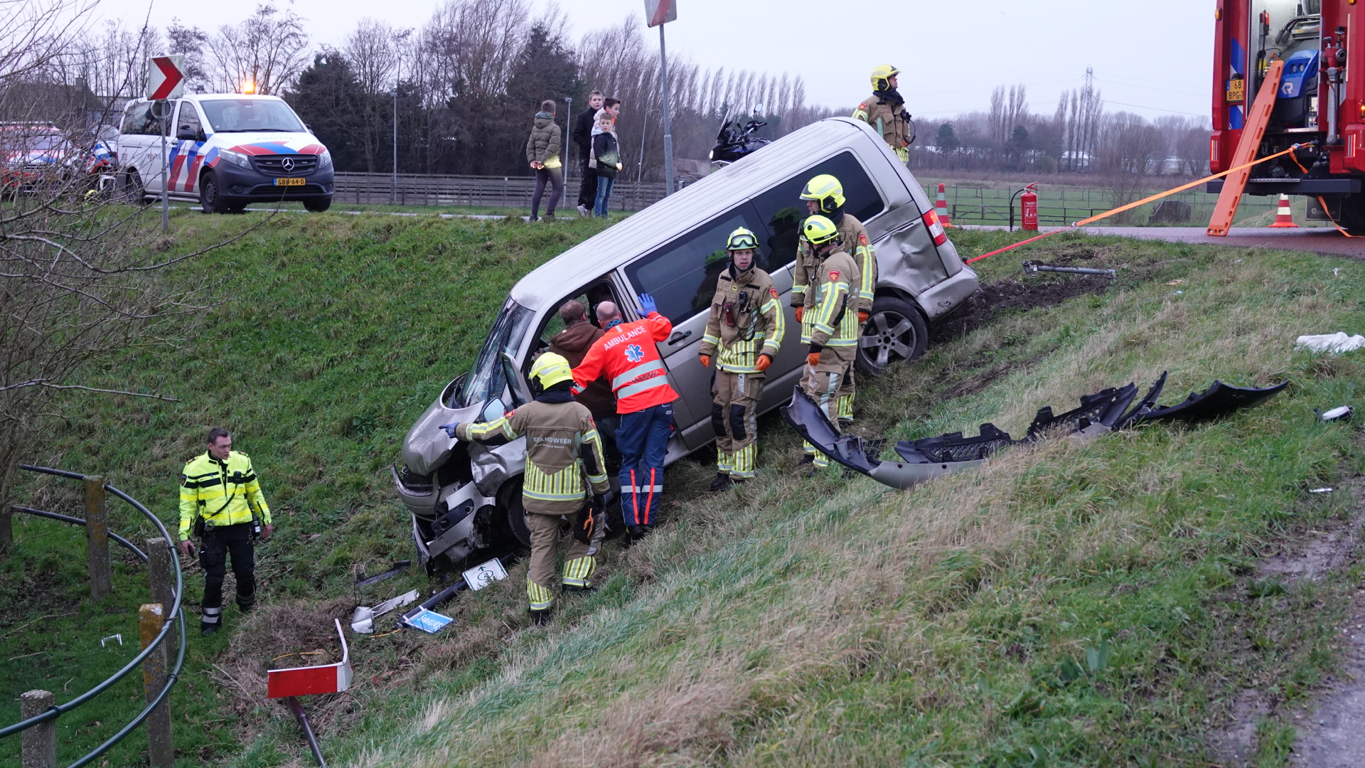 Hulpverleners bij een busje dat in een berm gecrasht is, met politie- en brandweerpersoneel aanwezig.