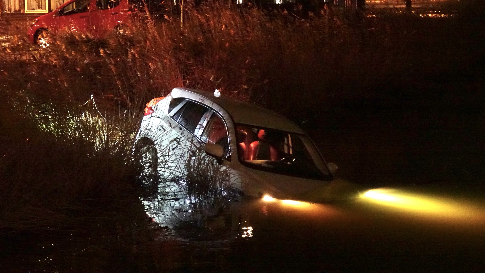 Auto met koplampen in water, deels ondergedompeld.