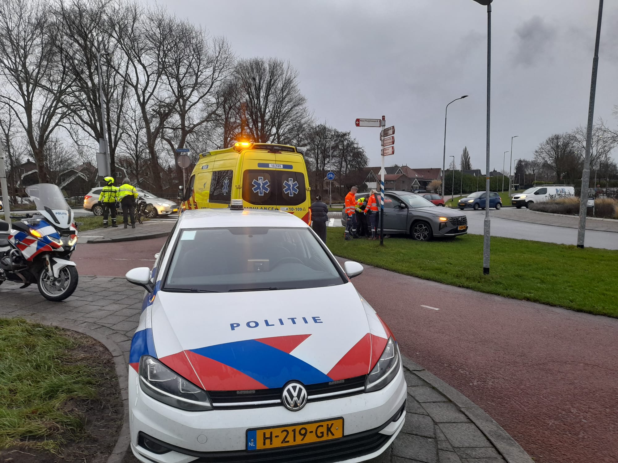 Politie- en ambulancevoertuigen bij een verkeersongeluk met betrokken personen op een kruising.