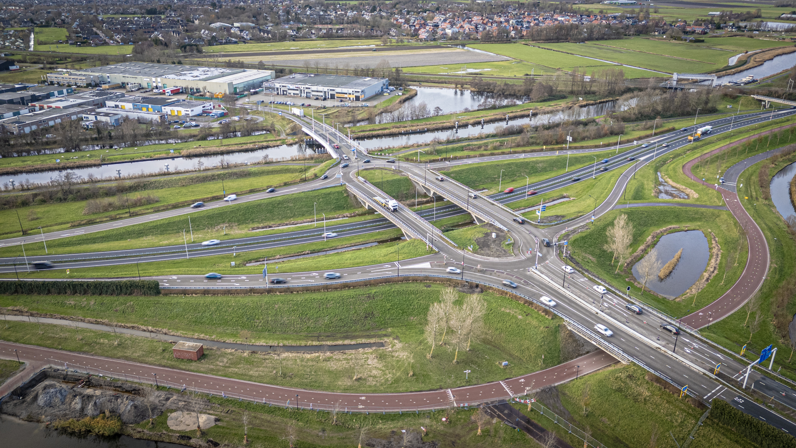 Luchtfoto van een verkeersknooppunt met snelwegen, wegen en fietspaden, omgeven door groen en water.