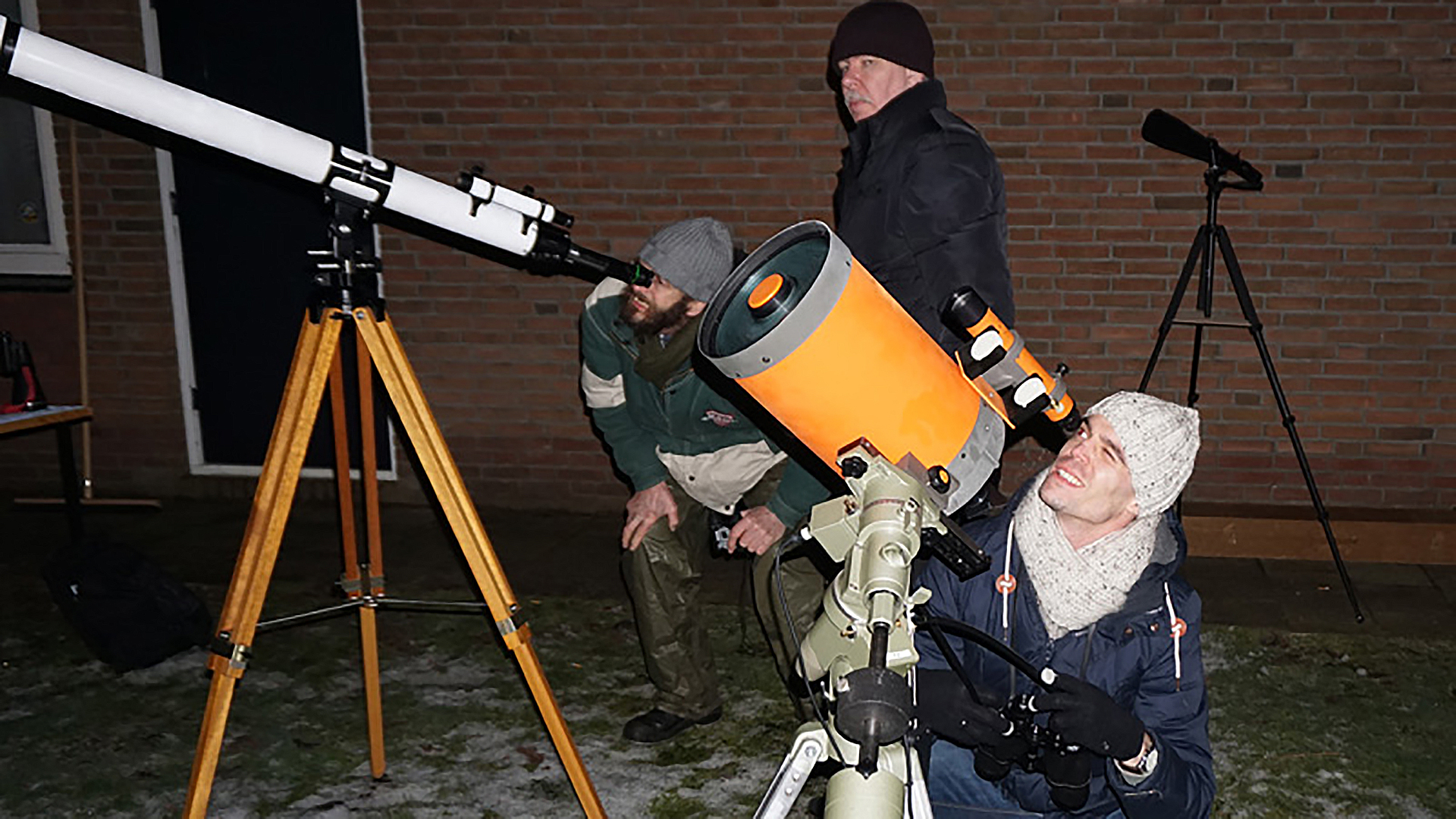 Drie mensen observeren de nachtelijke hemel met behulp van telescopen.