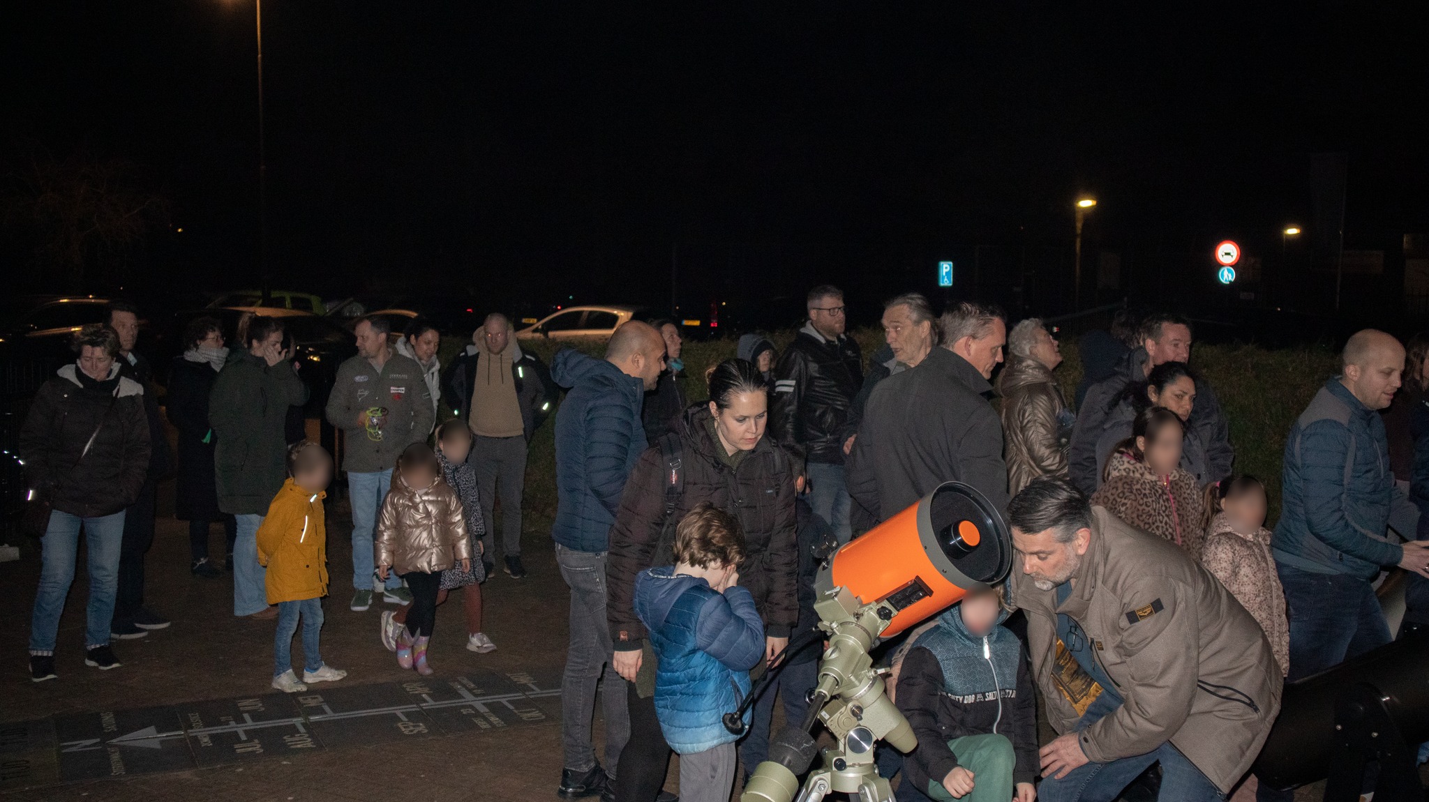 Groep mensen kijkt 's nachts naar een telescoop op een buitenlocatie.