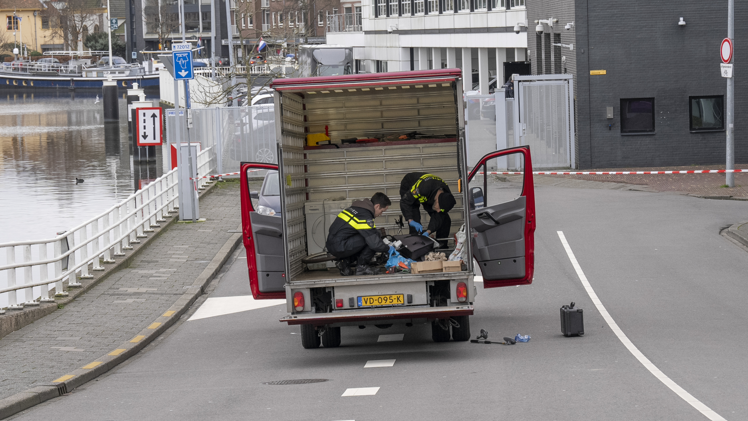 Twee personen in uniform onderzoeken de inhoud van een open bestelwagen met rode deuren op straat.