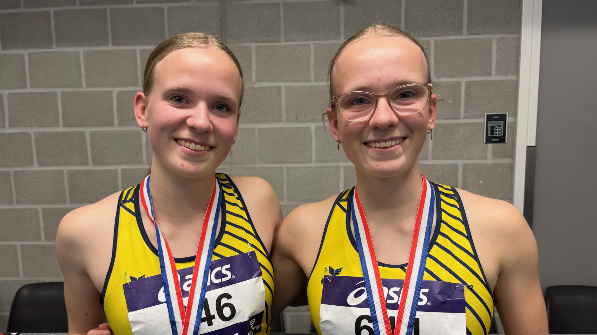 Twee jonge vrouwen in gele sportkleding met medailles om hun nek lachen naar de camera.