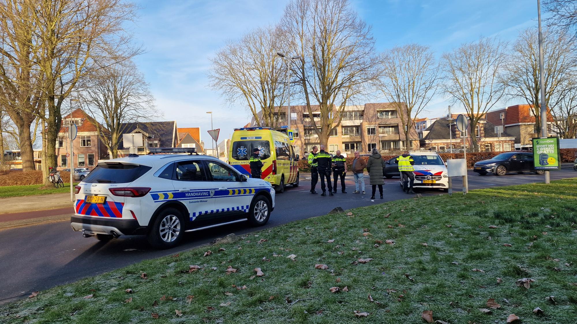 Opschudding op straat met politie, handhaving en ambulance aanwezig; meerdere personen staan erbij.