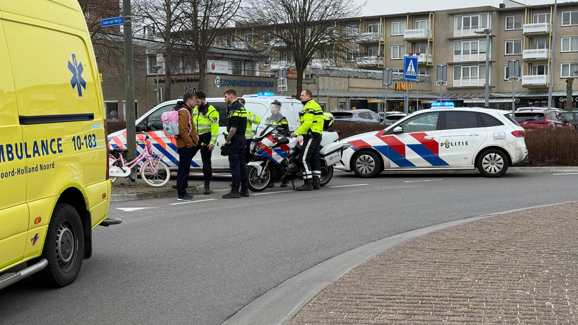 Politieagenten en een man staan bij een politieauto en motorfiets op straat naast een ambulance.