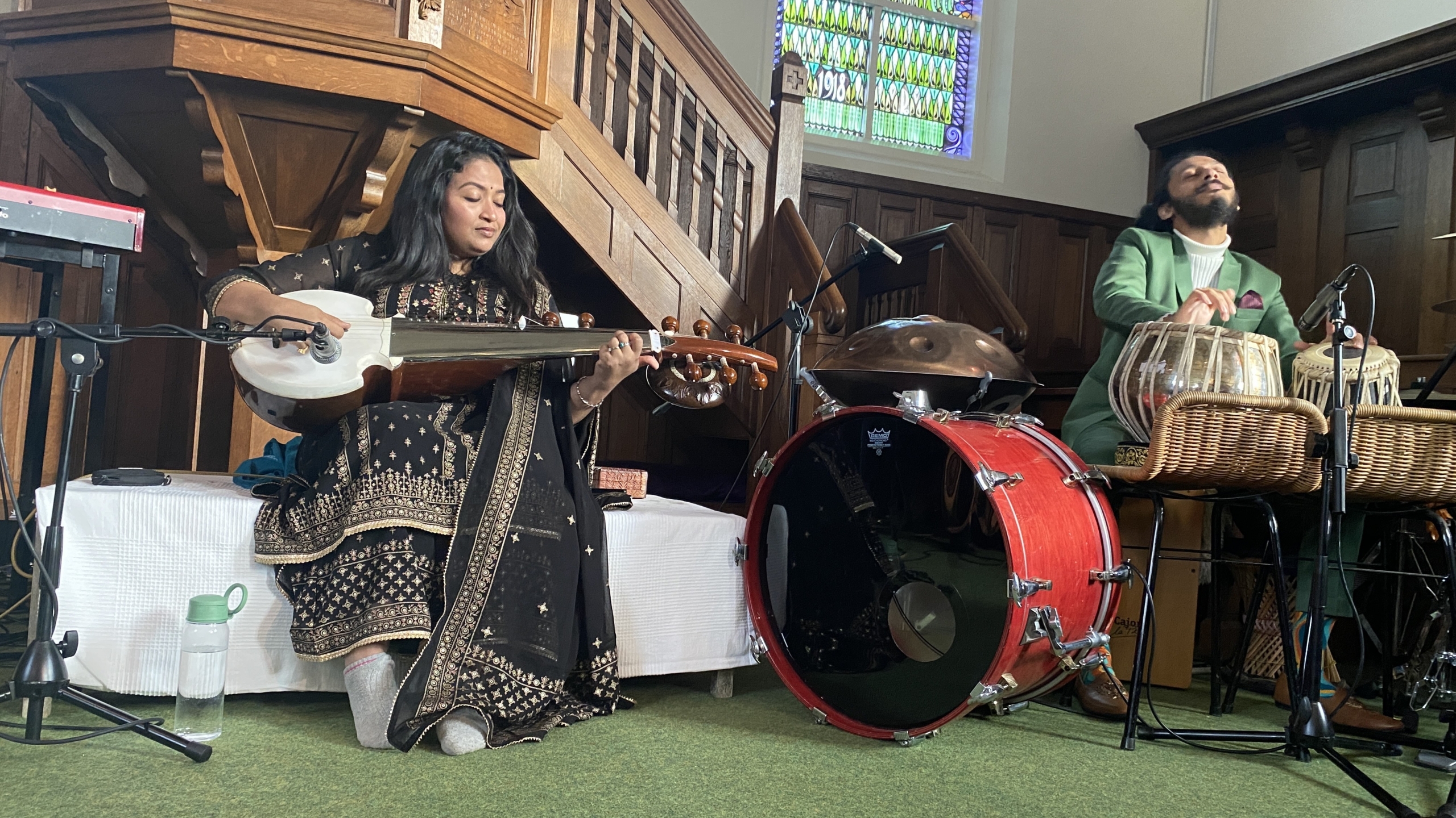 Twee muzikanten spelen traditionele instrumenten in een kerk met houten interieur en glas-in-loodraam.