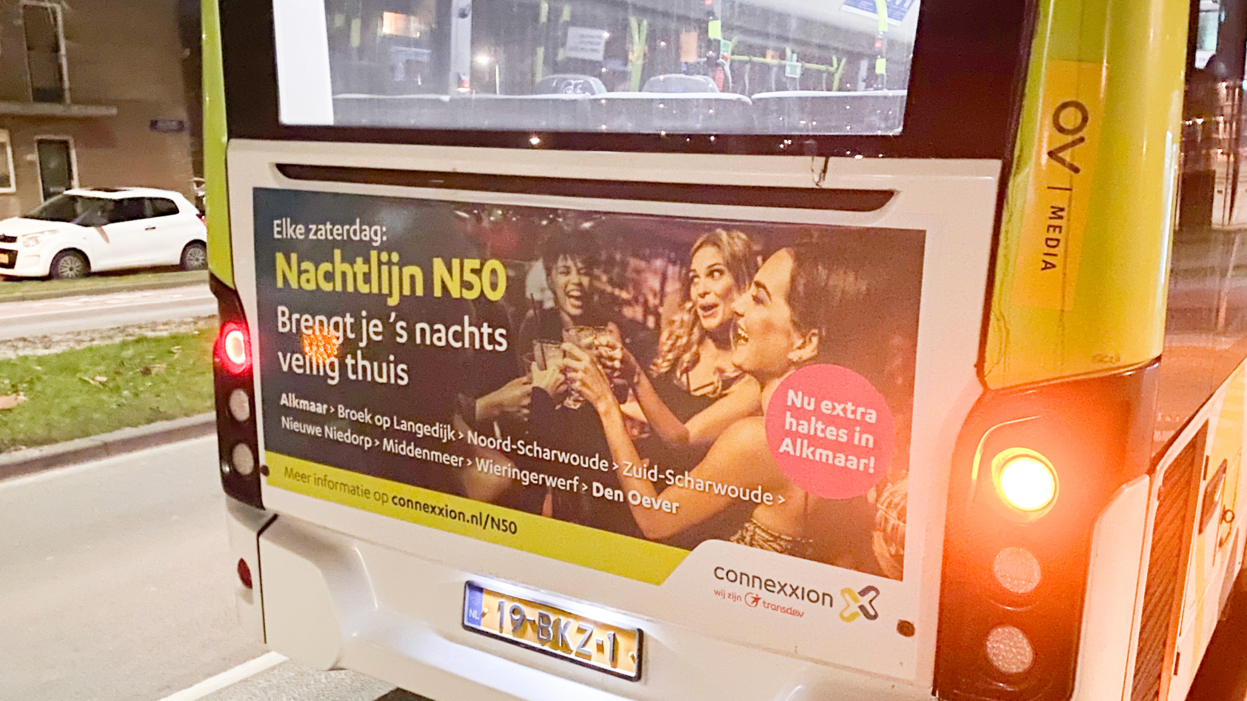 Achterkant van een Connexxion bus met een advertentie voor de Nachtlijn N50, met tekst die aangeeft dat de bus elke zaterdag 's nachts veilig naar huis rijdt en extra haltes in Alkmaar heeft.