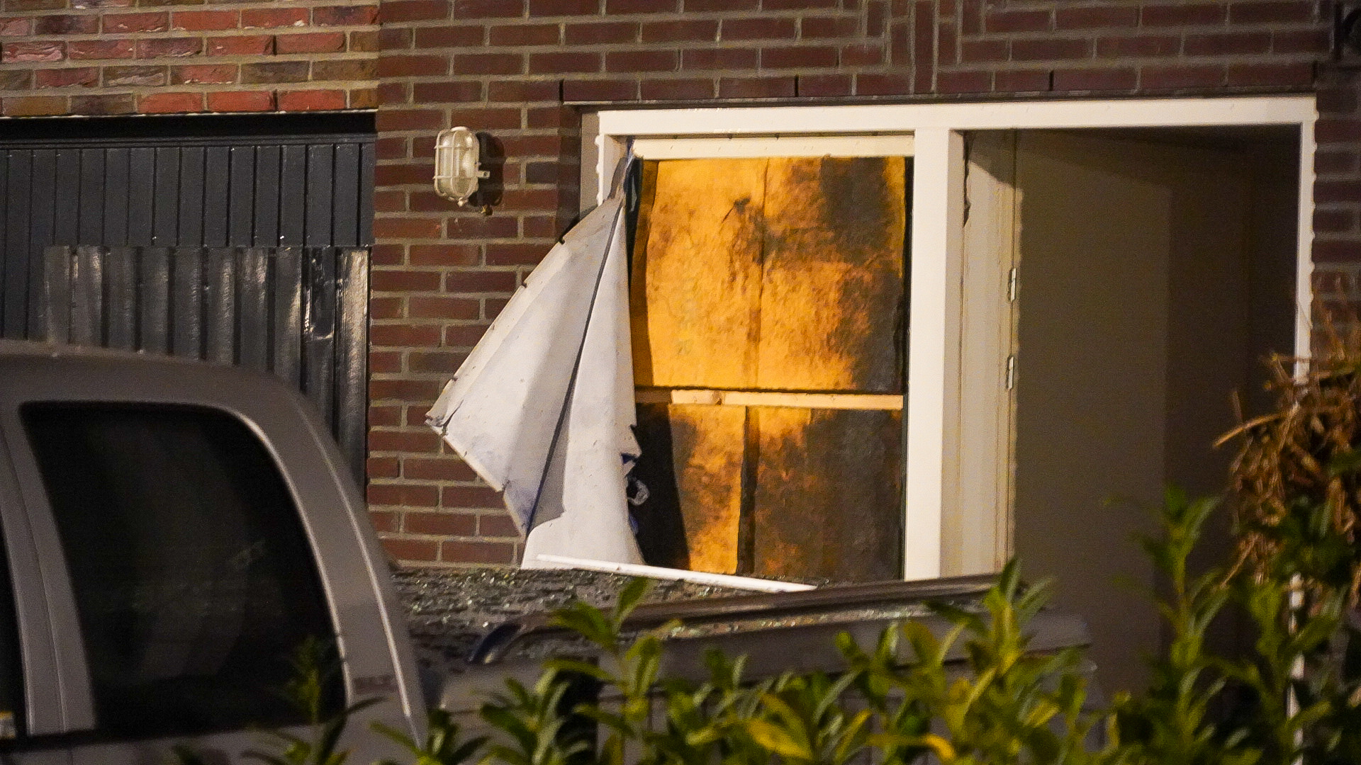 Kapotte deur met doorzichtig plastic in een bakstenen muur, nachtscène met verlichting van binnenuit.