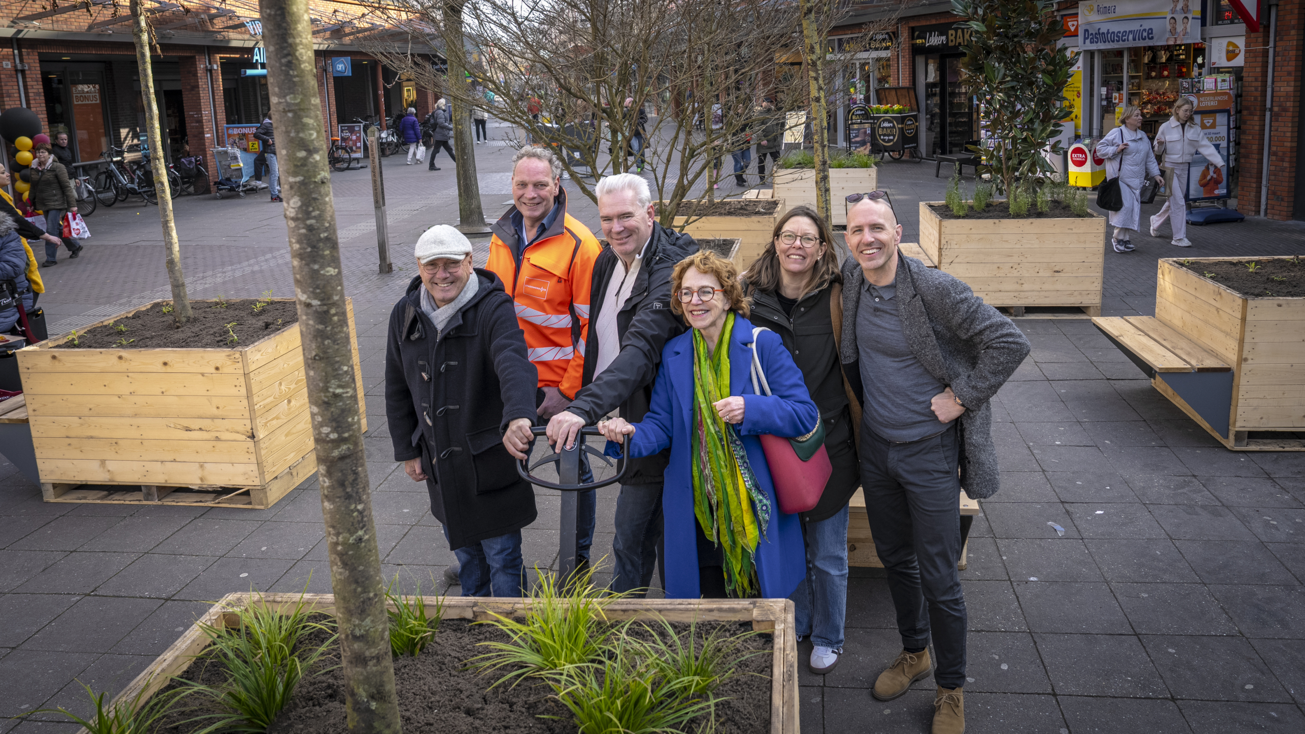 Groep mensen poseren bij houten plantenbakken op een plein.