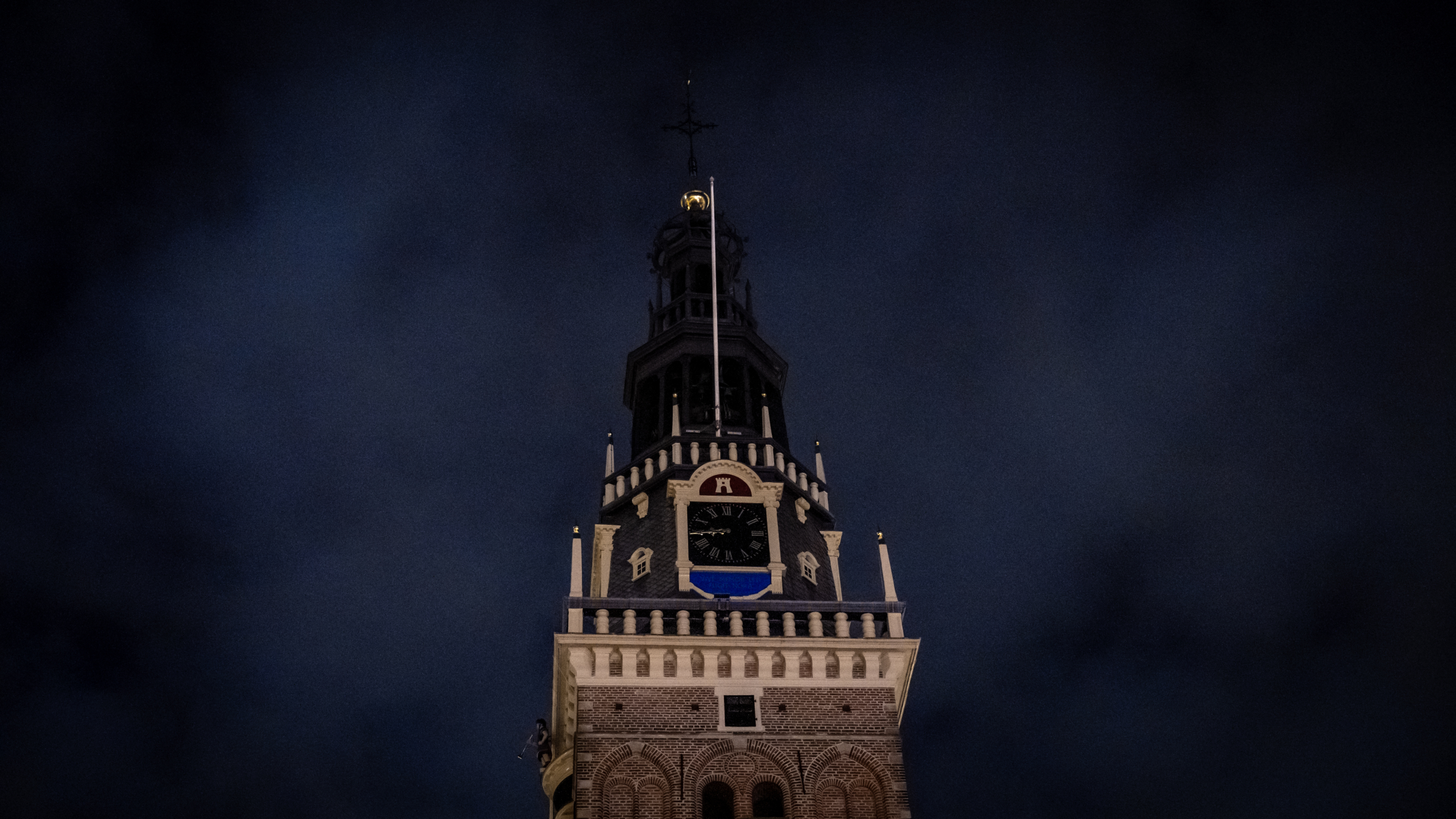 Klokkentoren van een historisch gebouw 's nachts, met verlichte wijzerplaat en donkere wolkenlucht.