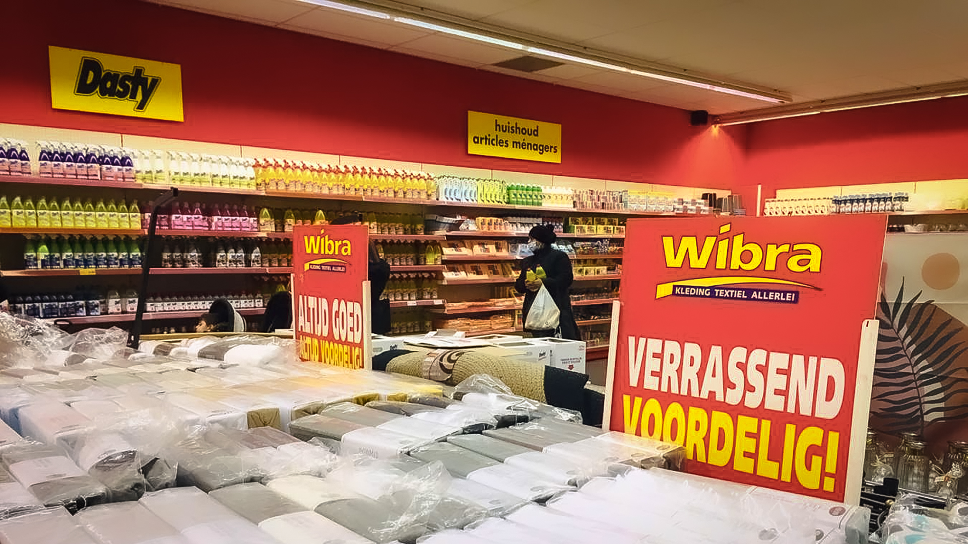 Winkelinterieur van Wibra met schoonmaakproducten en tekstiel in de aanbieding, met opvallende rode borden met reclame.