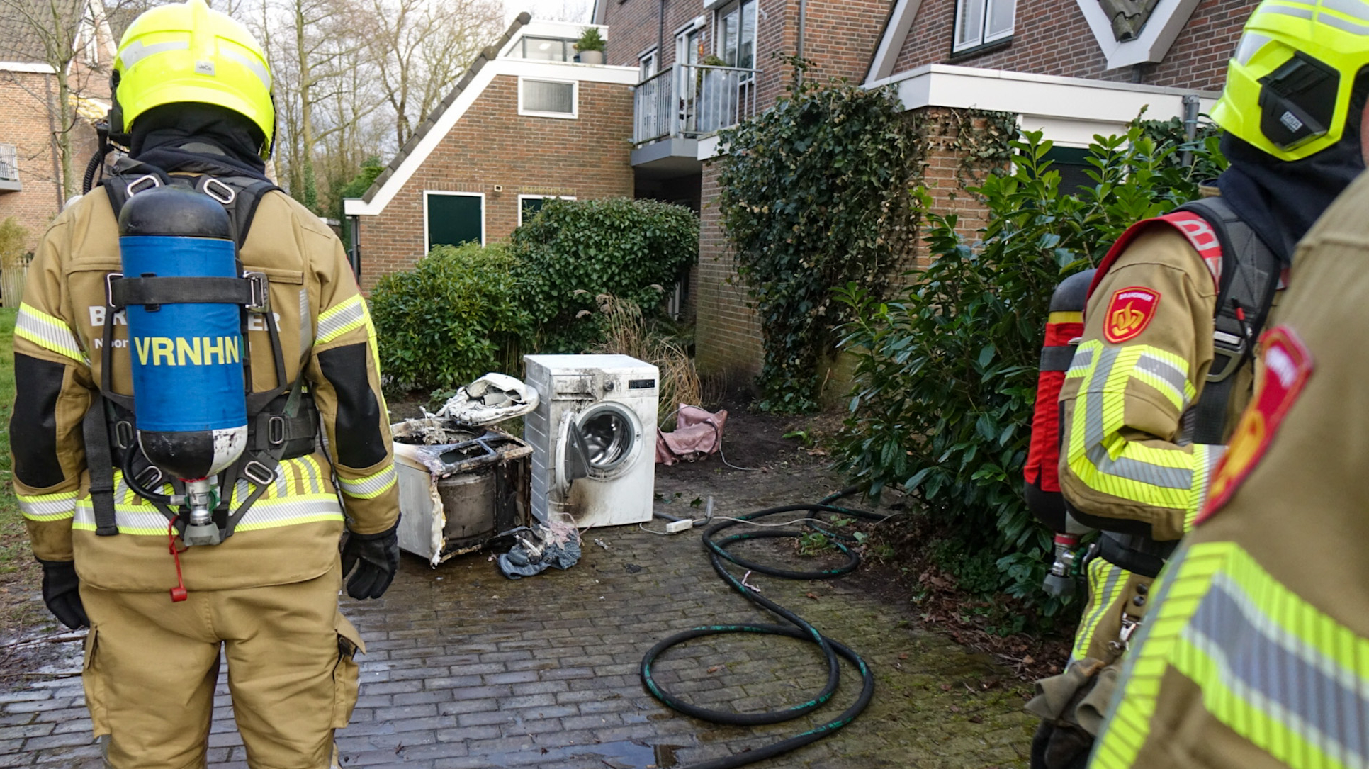 Brandweermannen bij uitgebrande wasmachines naast een gebouw.