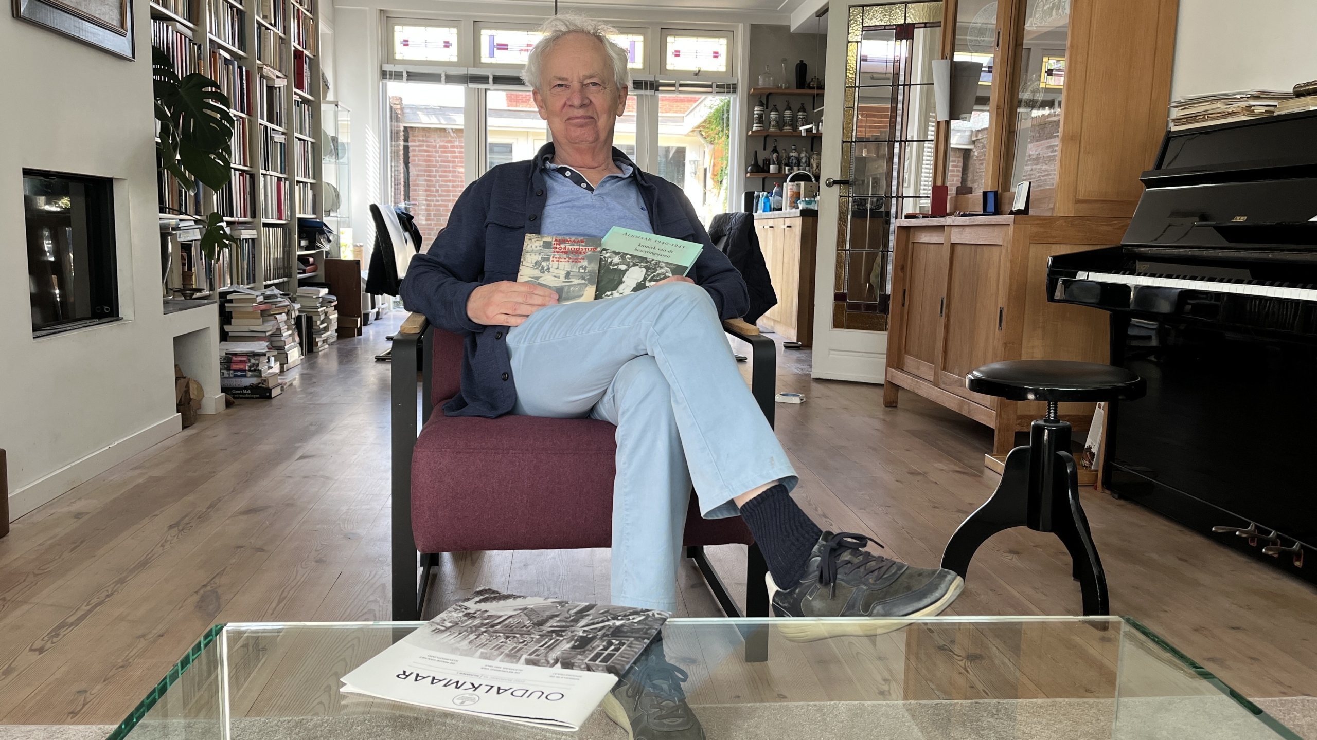 Gerrit Valk in zijn zitstoel met zijn boek Alkmaar in oorlogstijd en nog een ander werk van hem in zijn handen (foto: Streekstad Centraal)