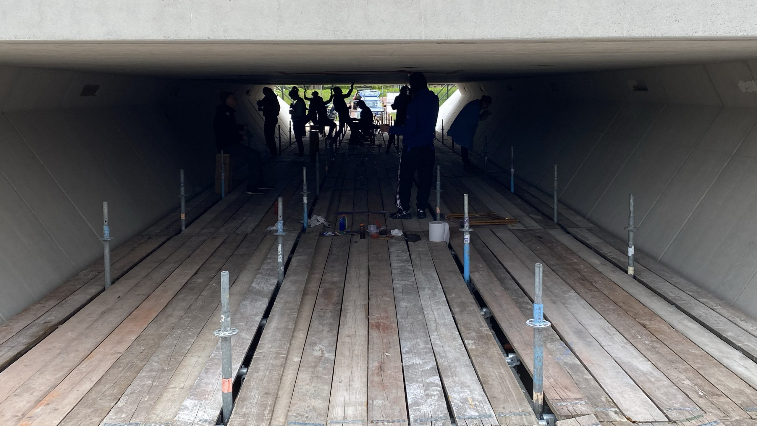 Mensen werken onder een brug met houten planken en steunen op de grond.