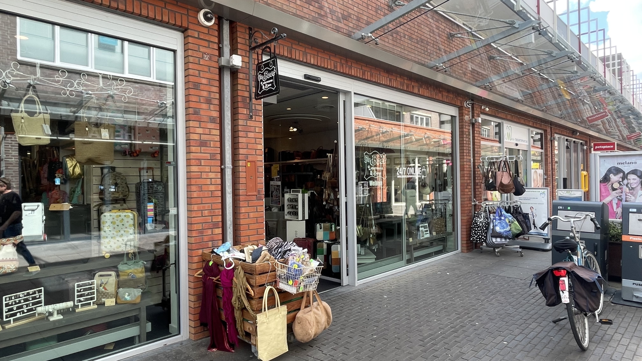 Winkel met een glazen voorgevel met tassen en bagageartikelen in de etalage en een fiets met tassen aan weerszijden geparkeerd op het trottoir ervoor.