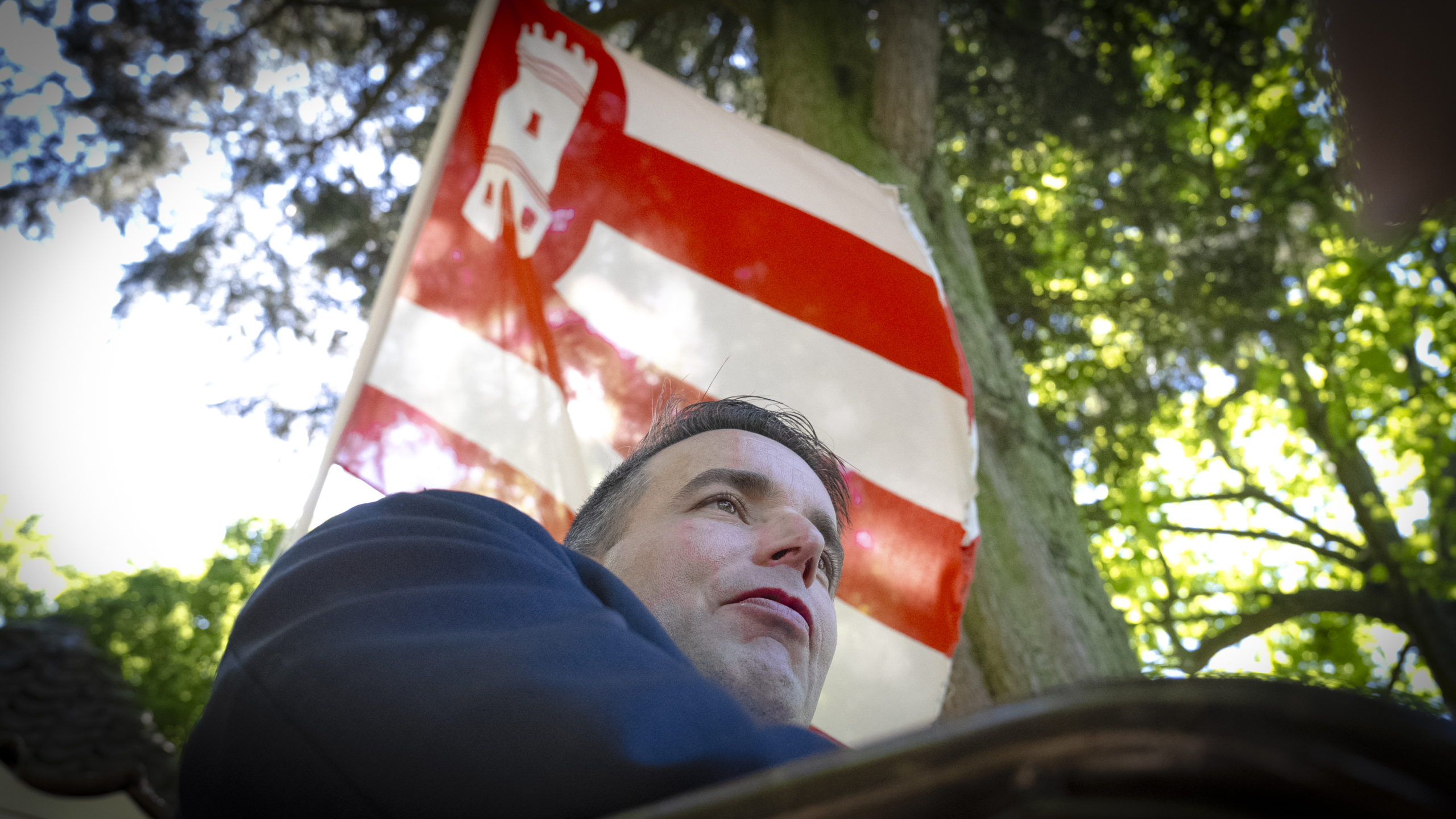 Een persoon staat onder een rood en wit gestreepte vlag met een torensymbool erop, in een bosrijke omgeving.