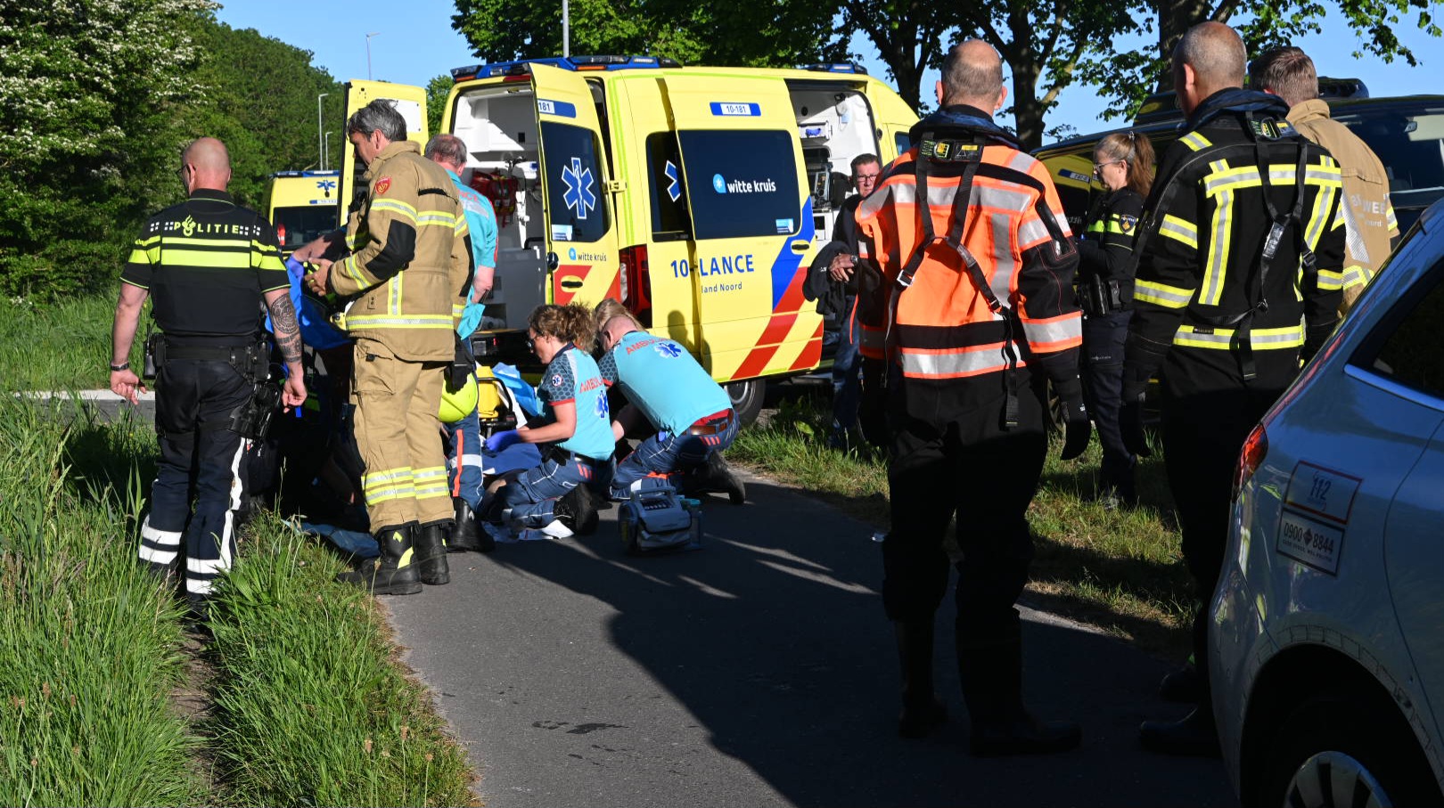 Hulpverleners van politie, brandweer en ambulance zijn aanwezig bij een noodgeval langs de weg naast een ambulance.