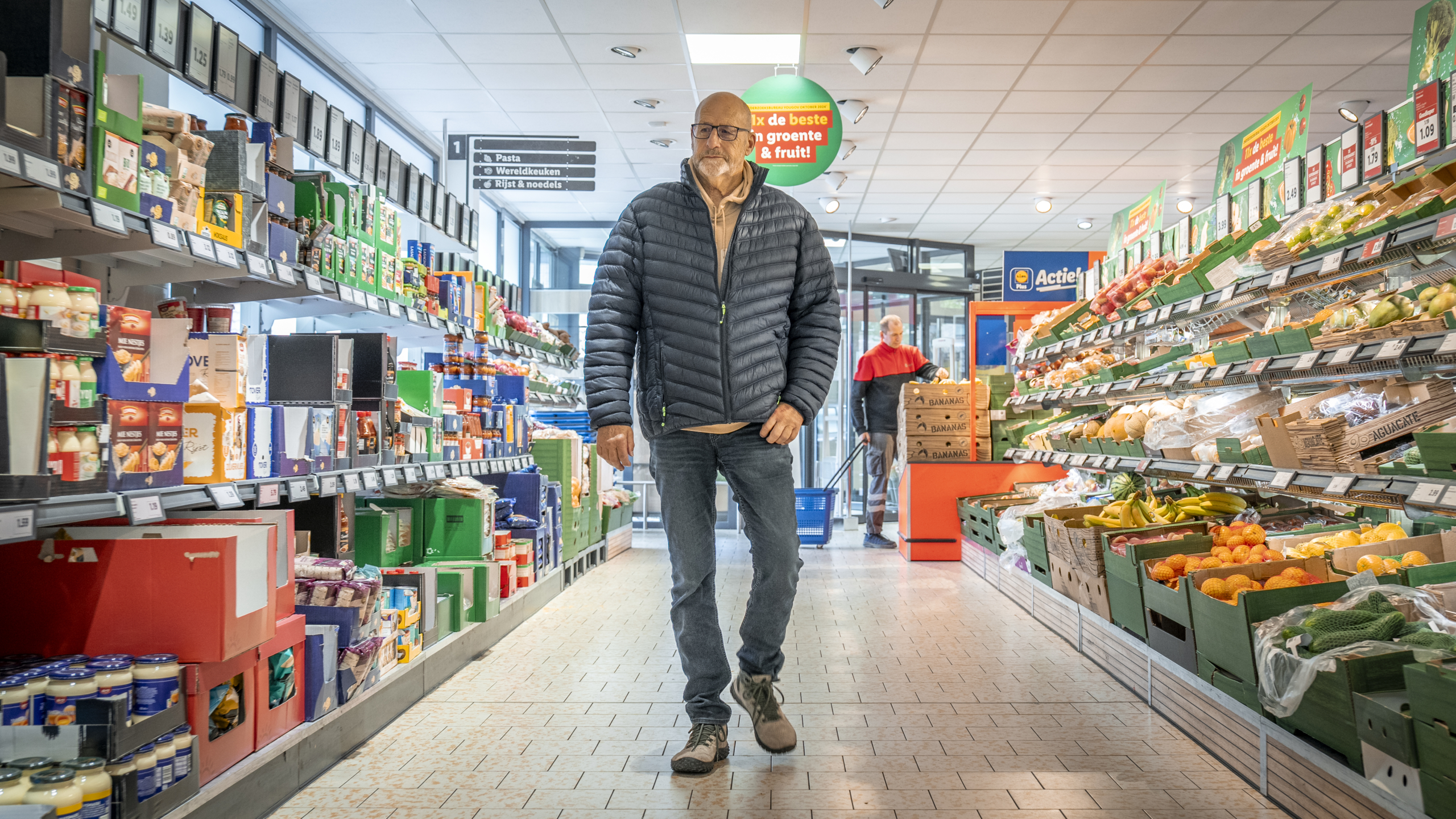 Man loopt door een supermarktgang met aan weerszijden schappen vol producten.