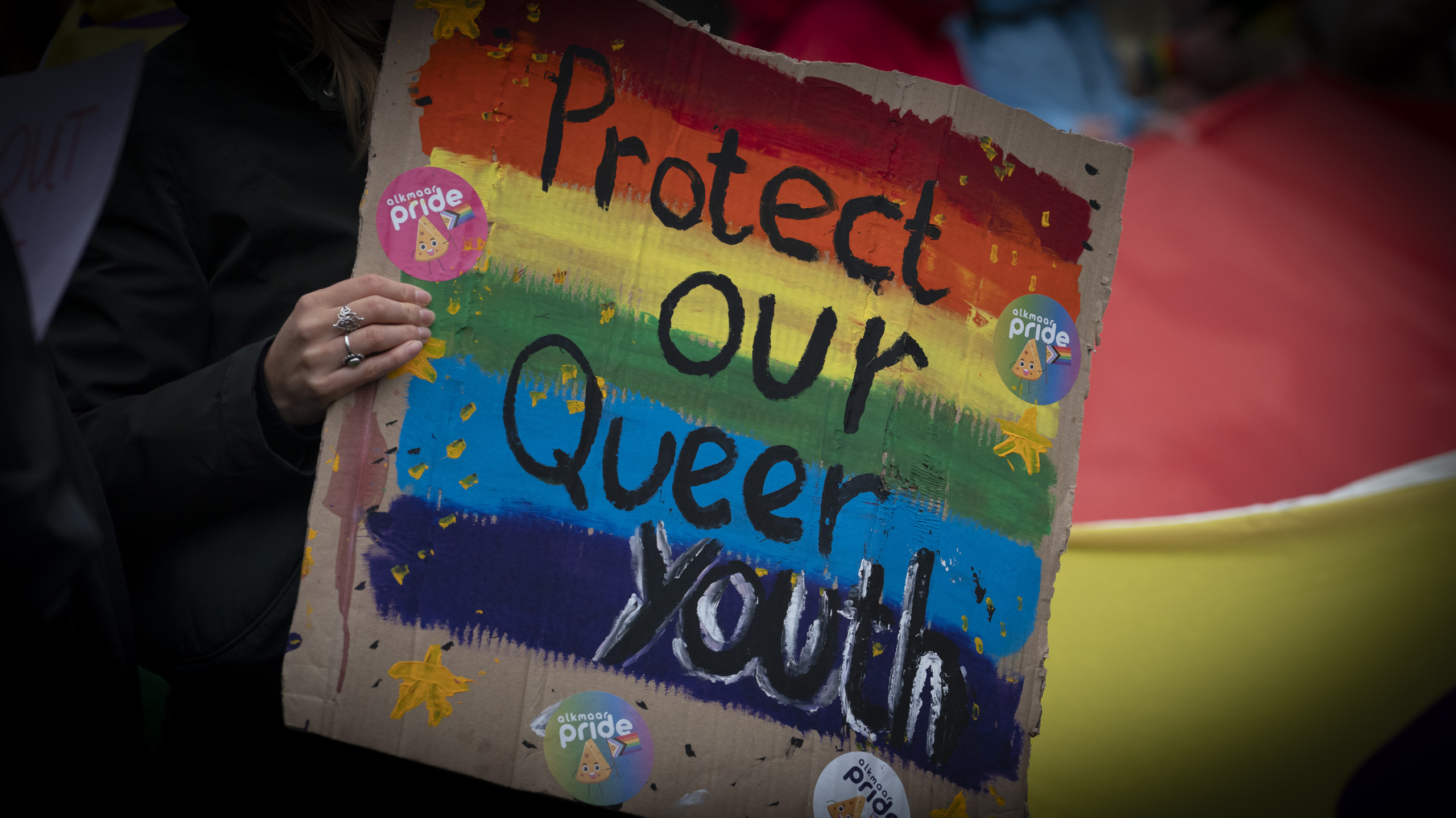 Bord met regenboogkleuren en de tekst 'Protect our Queer Youth', met Alkmaar Pride-stickers.