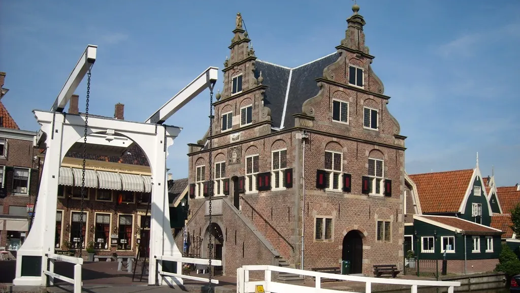 Historisch gebouw in traditionele Nederlandse stijl met trapgevels, naast een witte ophaalbrug, in een zonnige straat.