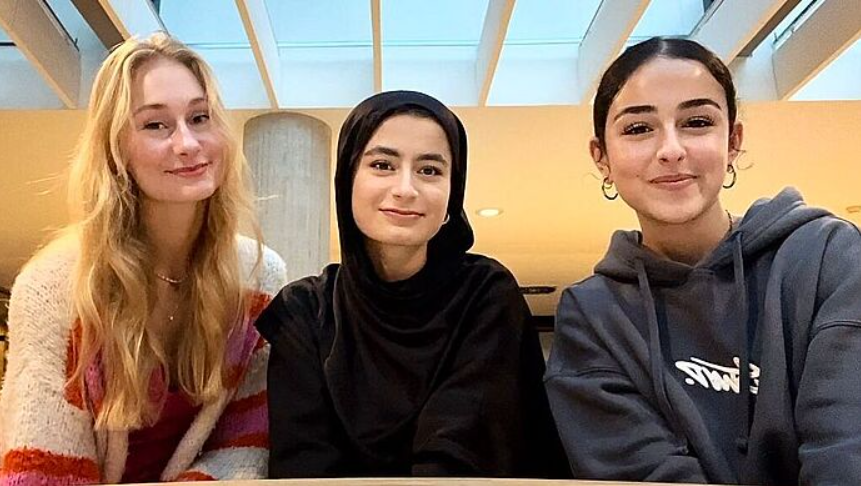 Drie jonge vrouwen glimlachen terwijl ze samen poseren in een kamer met een glazen plafond.
