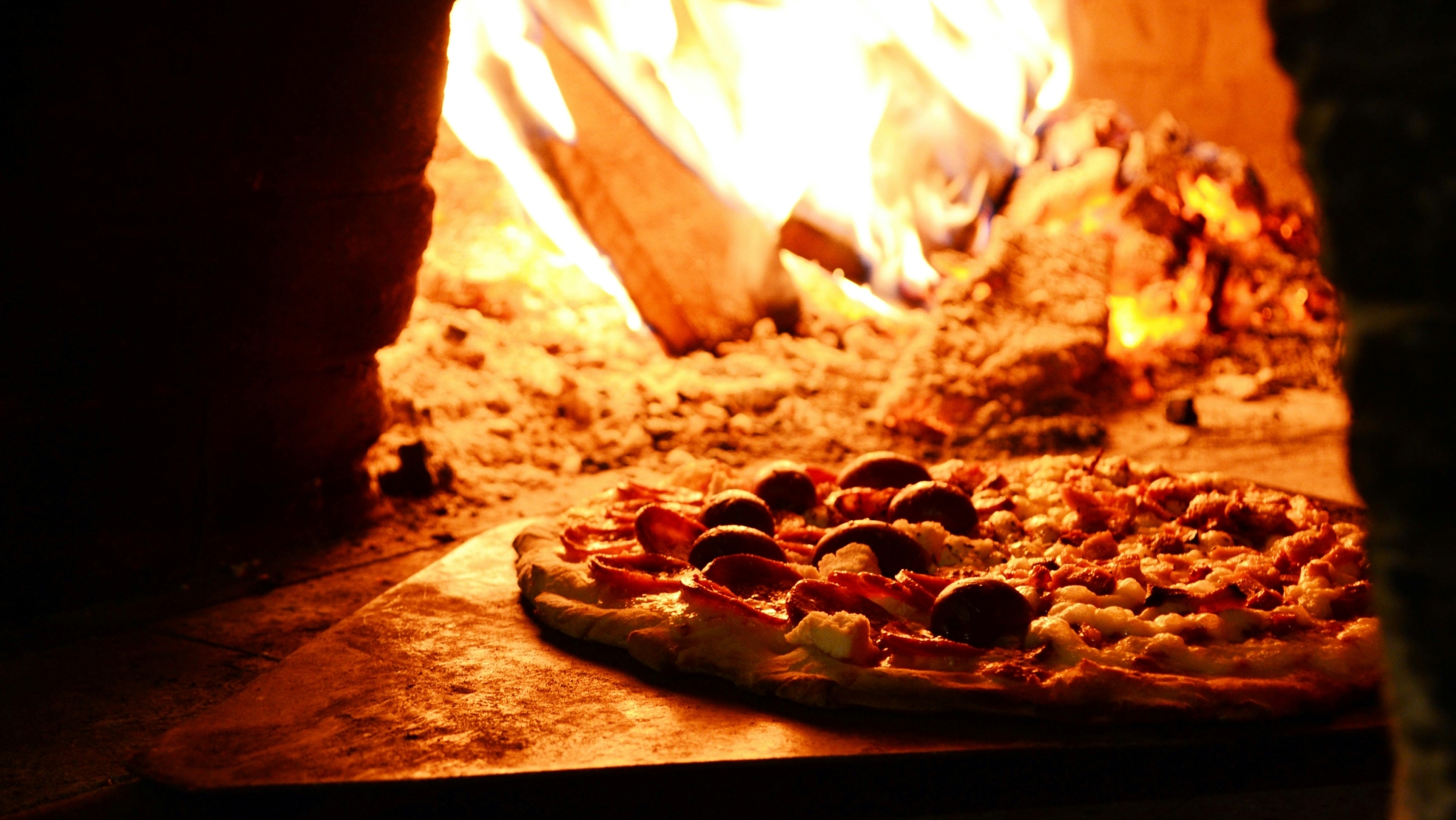 Pizza in een houtgestookte oven, met een vlam op de achtergrond.